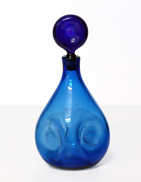 Teardrop bodied decanter with four circular ipressions and indented doughnut-like disk stopper, designed by Wayne Husted in 1959, made for 2 years only.
Design #5932 in Persian, pictured in the 1959 catalog on the first color plate