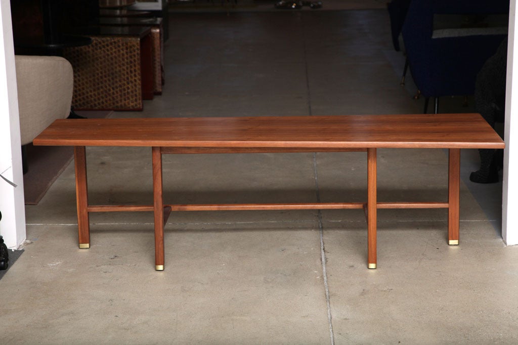 Coffee table by Edward Wormley for Dunbar. USA, circa 1950. Trapezoid-shaped top on a simple base with brass capped feet. Natural walnut finish. 