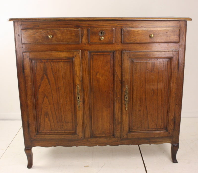 A taller antique patinated buffet from France, good narrow depth. Elm with particularly nice color and graining. Note the shaped feet and scalloped apron, raised panels on the cabinet doors, and paneled sides. Original escutcheons. Three drawers