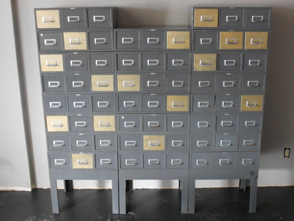 This steel card catalog by Cole Steel consists of three separate banks, each bank stacked with 3-drawer units that connect to each other by hooks in back. The drawers slide easily in-and-out and can be arranged in a checkboard pattern of tan and