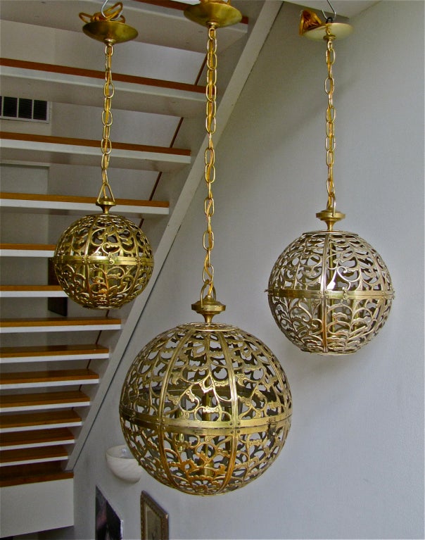 Trio of high quality pierced brass pendants in graduated sizes with scroll motif. Rewired with new triple cluster light sockets and solid brass fittings. Ceiling drop can be adjusted as needed. Each pendant uses 3 - 40 watt max candelabra base