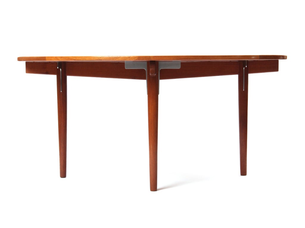A round teak dining table on tapered dowel legs with chrome plated steel corbels.