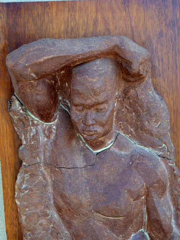 This unusual wall sculpture depicting a nude male is composed of three separate ceramic slabs mounted on a large walnut board. The subject's well defined physique emerges in the classic contrapposto stance from a background of roughly rendered clay.