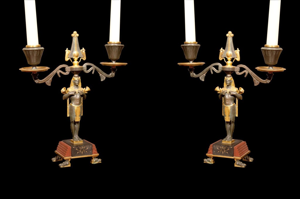 # C113 - Pair of Egyptian Revival bronze and ormolu double arm candlesticks in the Empire taste. A finely cast pharoah figure holds lotus blossoms and supports on his head the double candlearm with a Egyptian stylized finial. All resting on a black