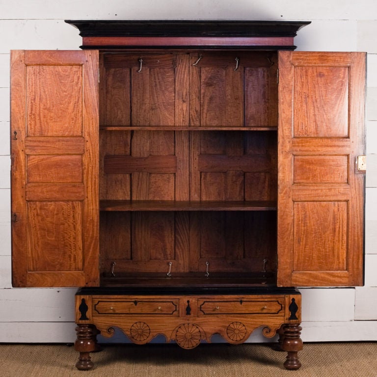 Indo-Dutch Colonial armoire on two drawer stand with ebony inlay. Satinwood raised panel doors with ebony inlay. Base has flush front drawers with small brass pulls. Top portion of the cabinet collapses for easy transport.