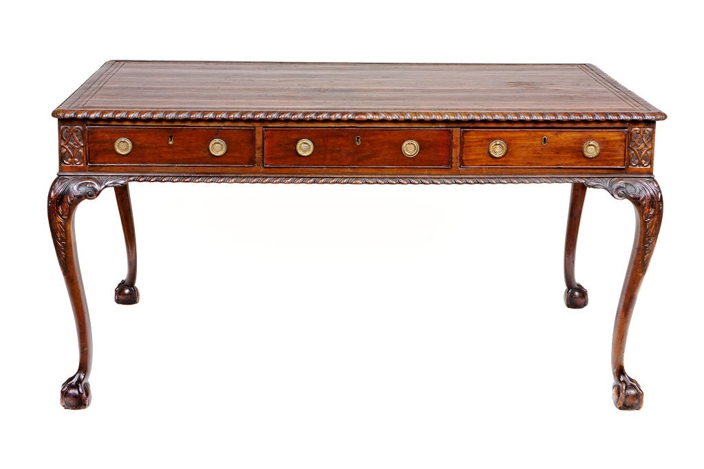 George III Style carved mahogany writing table, the rectangular top enclosing a gilt tooled leather insert.  The frieze with three opposing drawers on carved on carved cabriole legs, supported on claw and ball feet.