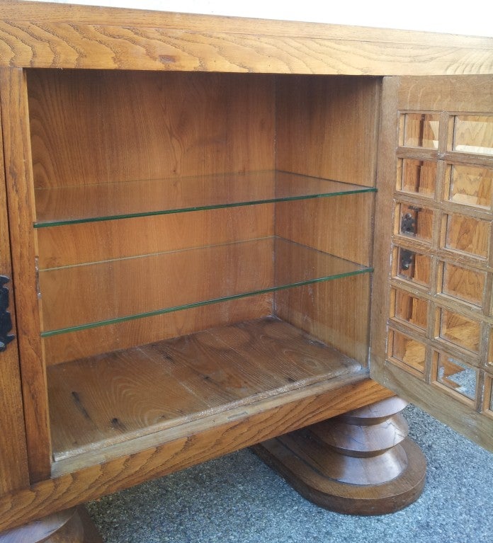 Piece of furniture 1930 of Charles Dudouyt's arrangement in massive ash tree opening on three doors. The central door is constituted by original set rectangles of beveled glass. The internal shelves are glass. The piece of furniture rests on massive