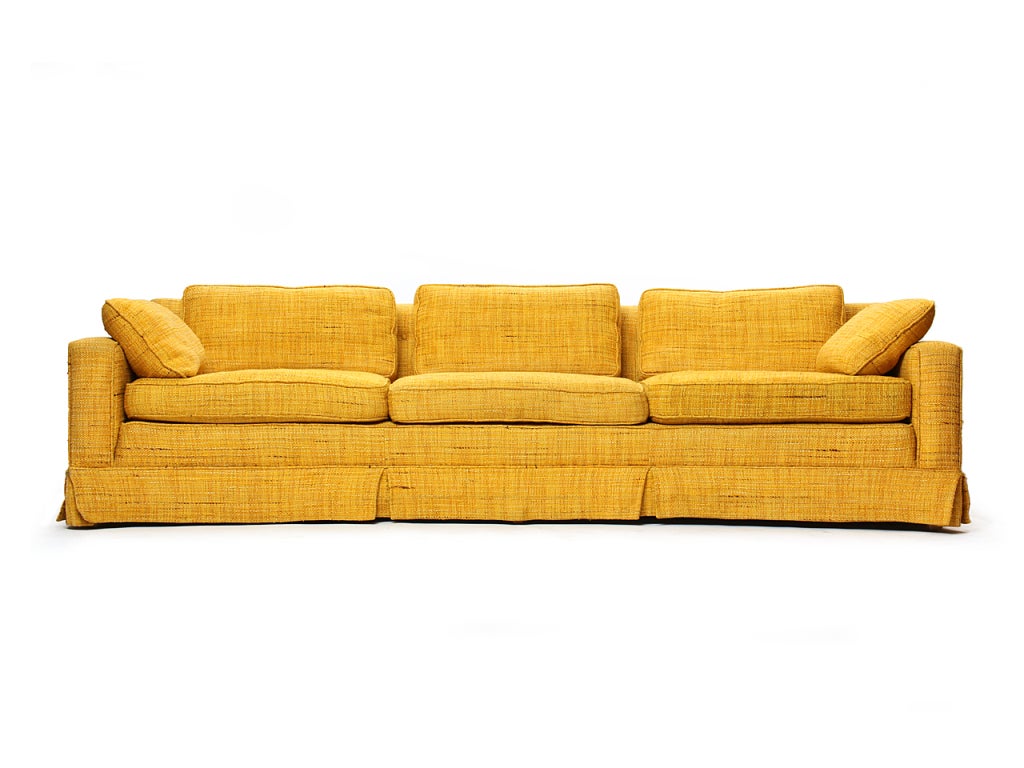 A three-set skirted arcing sofa in the original orange upholstery.