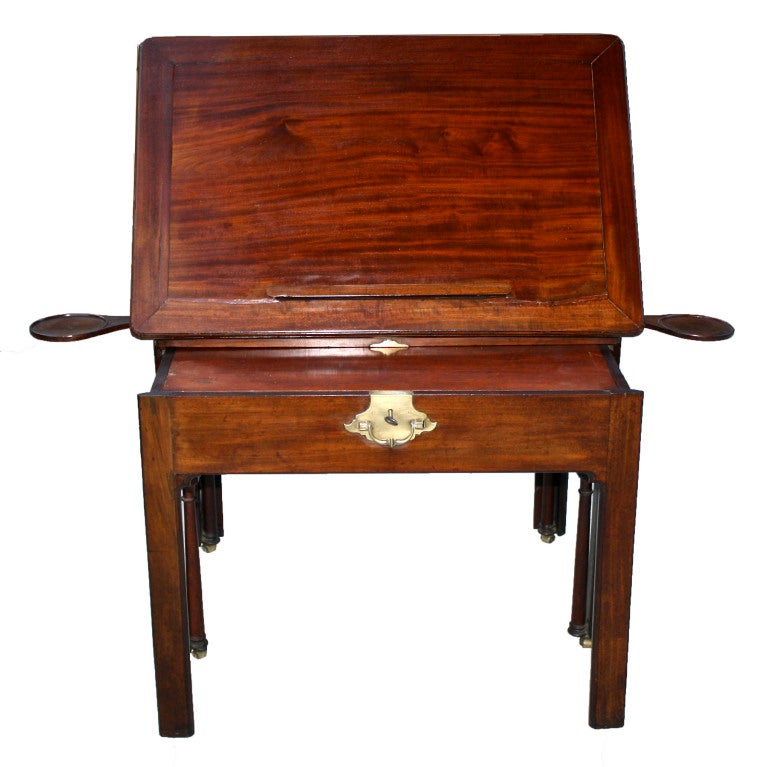 A rectangular hinged and ratcheted top with candle-slides to each side above a mahogany slide-covered drawer with a small hinged quarter-round drawer in the side; on two-sided square legs with engaged interior hidden turned columns on brass casters.