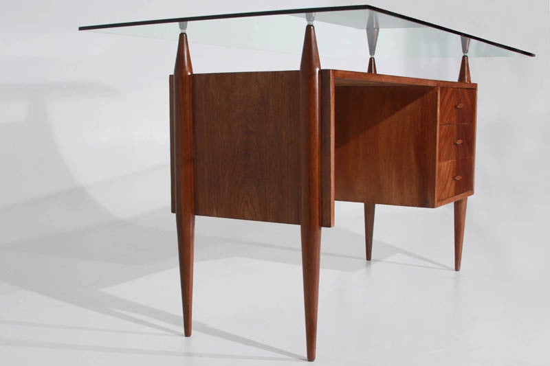 Sculptural Caviuna desk by Giuseppi Scapinelli with a floating glass top and three drawers. The legs extend upward to hold the glass top and are tapered (unequally) on both ends.

In order to preserve our inventory, after restoration we blanket