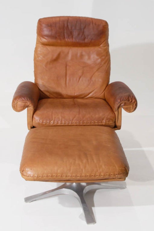 A De Sede distressed caramel leather armchair and ottoman with oversized, hand stitching and polished, solid cast aluminum legs that swivel. High quality Swiss materials and craftsmanship. Detached back and seat cushions are on molded plywood