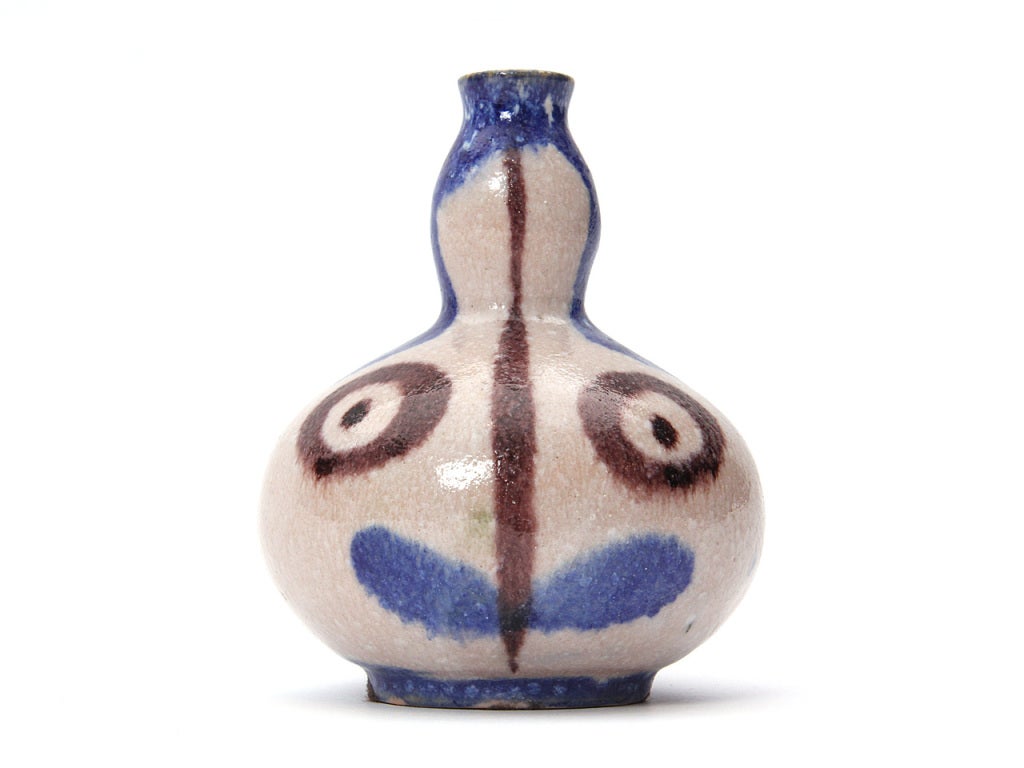 A petite hand thrown bud vase with an abstract face in white, blue, and brown glaze.