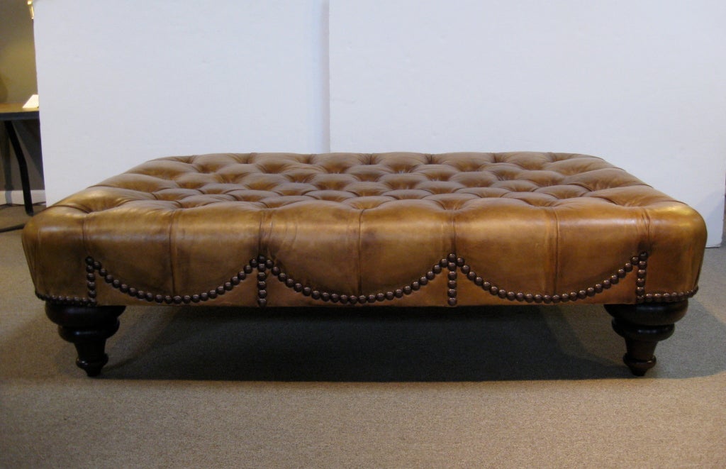 Oversized tufted leather ottoman by designer George Smith.  Featuring large turned wood legs, and decorative nail heads in a scalloped design.