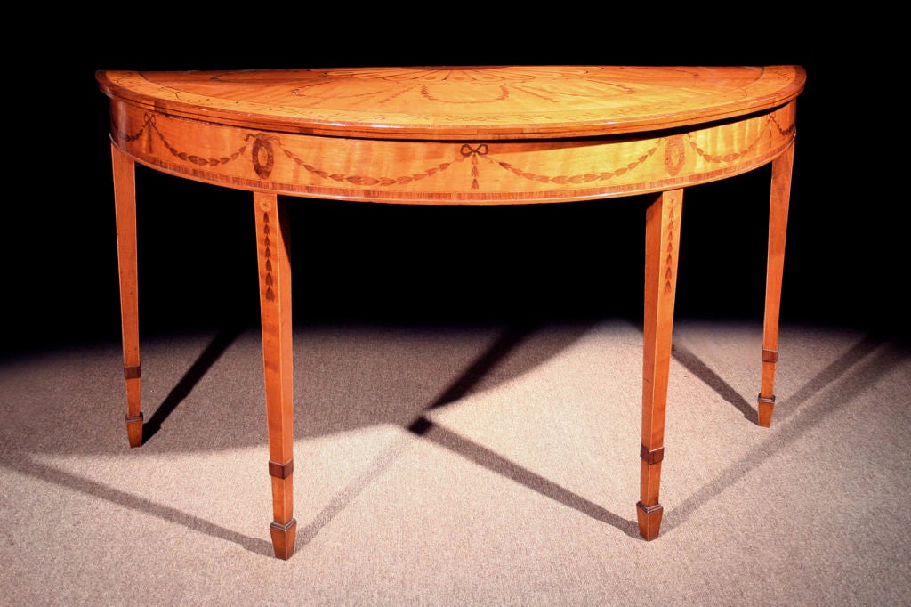 # A506 - Important George III half round side table executed in satinwood and enriched with beautifully detailed marquetry inlays. Inspired by the Neoclassical Revival in England, celebrated designers, such as George Hepplewhite (see his design