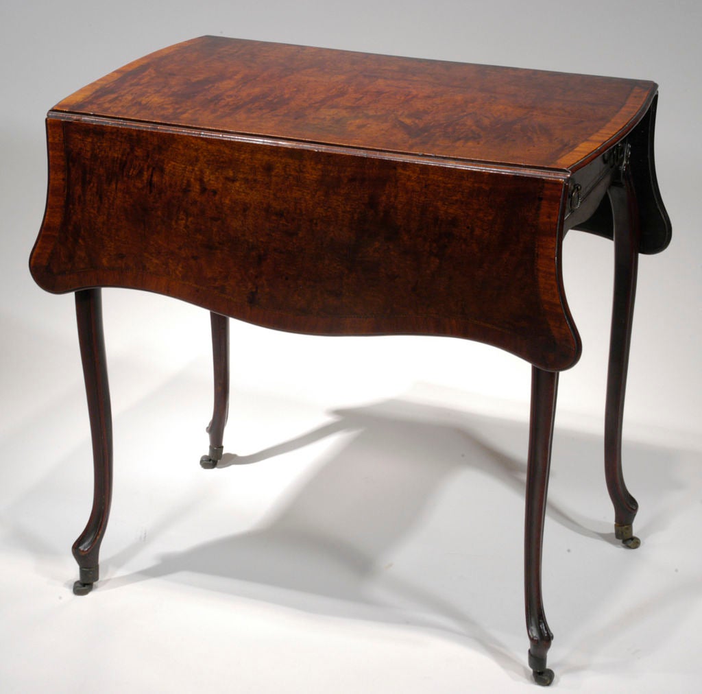 A very fine Chippendale period mahogany Pembroke table, with finely figured and crossbanded serpentine top, above a shaped apron with a single long drawer opposite a faux drawer, on four carved and shaped fluted cabriole legs carved to the tops with