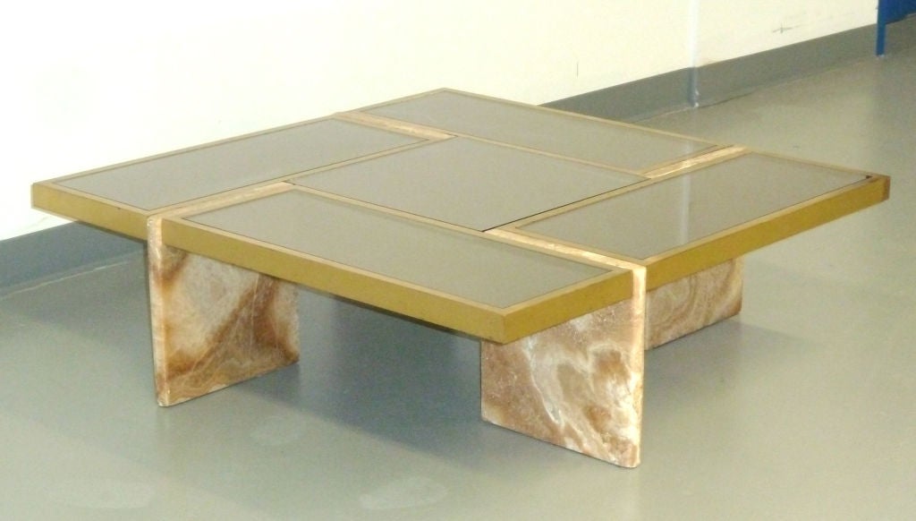 Geometric form low table sits on travertine slab legs with a brass grid top holding panels of smokey mirrored glass.