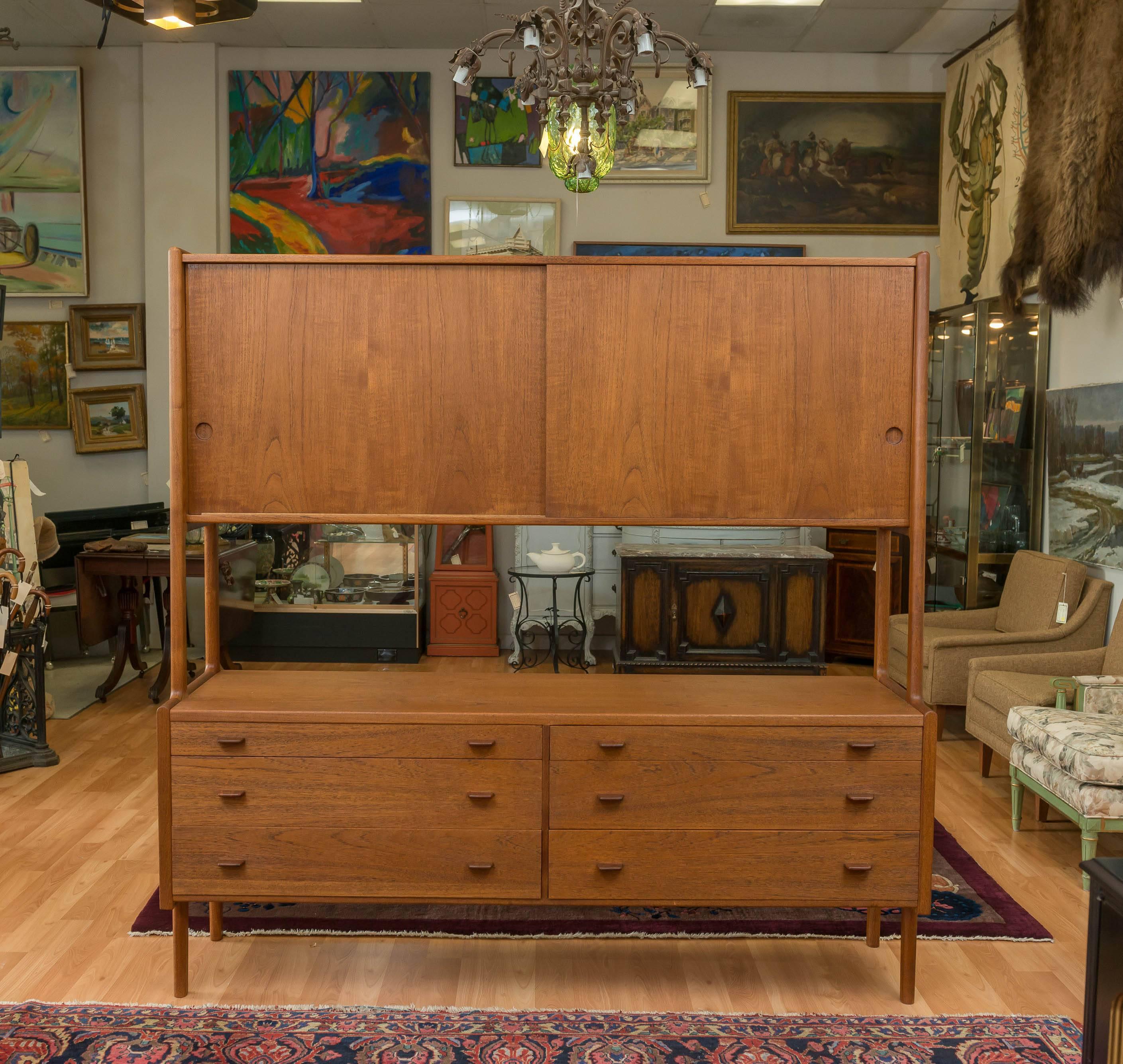 A large Hans Wegner designed Teak credenza, with enough storage space to hold it all. Upper unit has two sliding doors, behind those doors are four adjustable shelves. Lower unit has six pull tab drawers, with the top left drawer has a Green felt