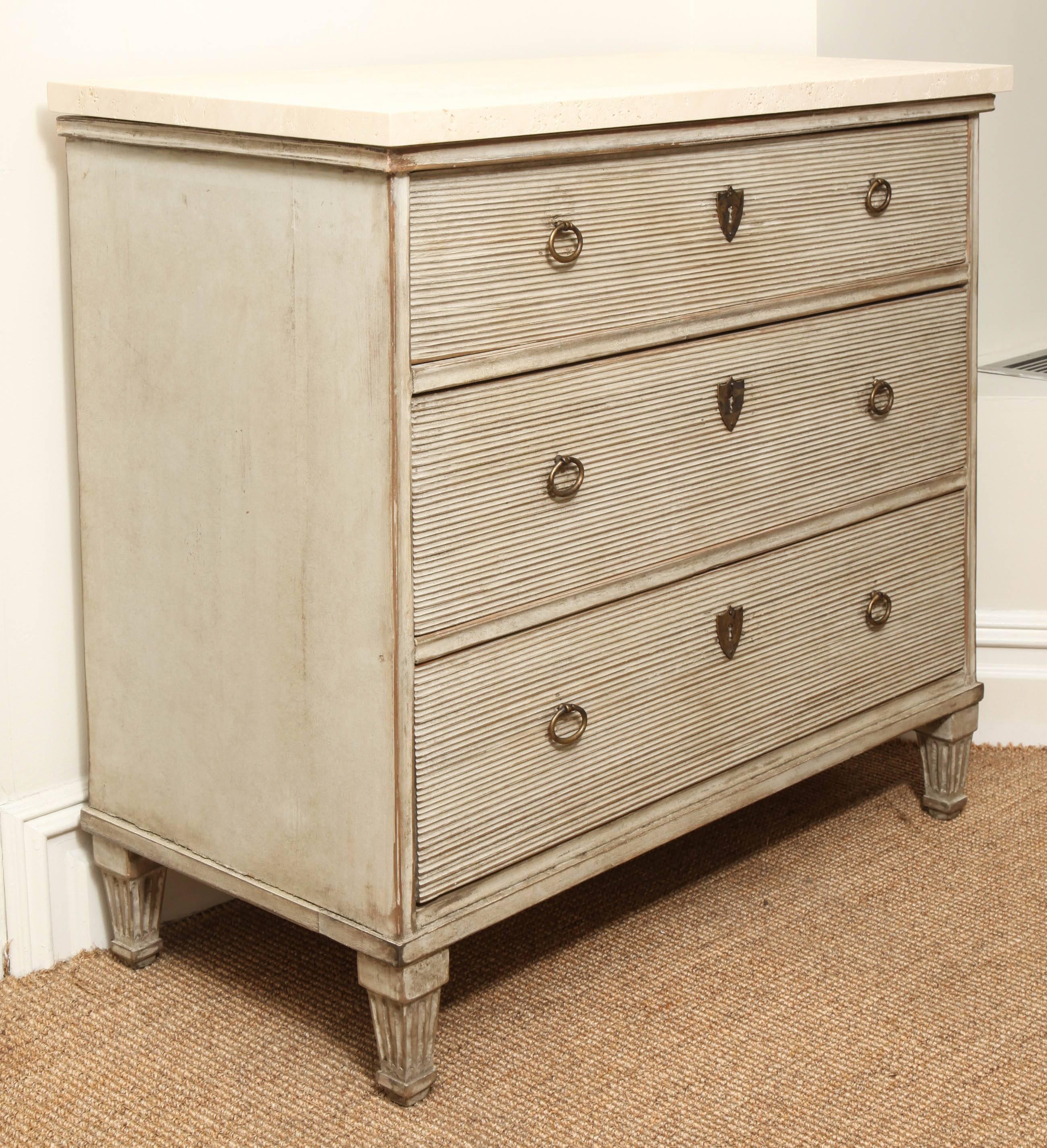 Painted three-drawer commode with ribbed drawers, tapered ribbed feet and travertine top.