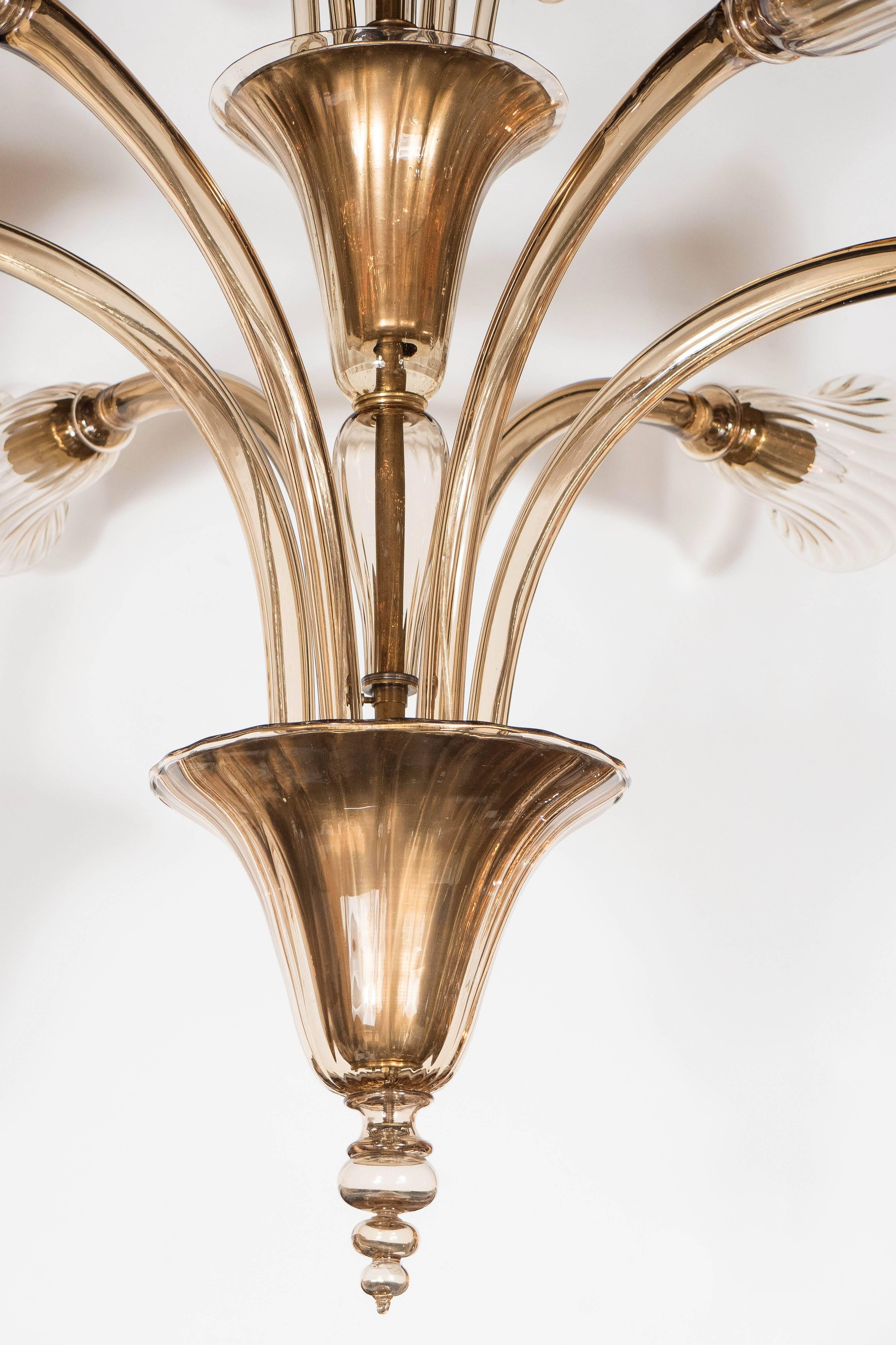 This elegant chandelier features six arms in stylized trumpet form on the lower tier and six rounded stylized tendrils in scroll design on the upper tier. The handblown Murano glass is an exquisite champagne color. Each of the arms emanates out of