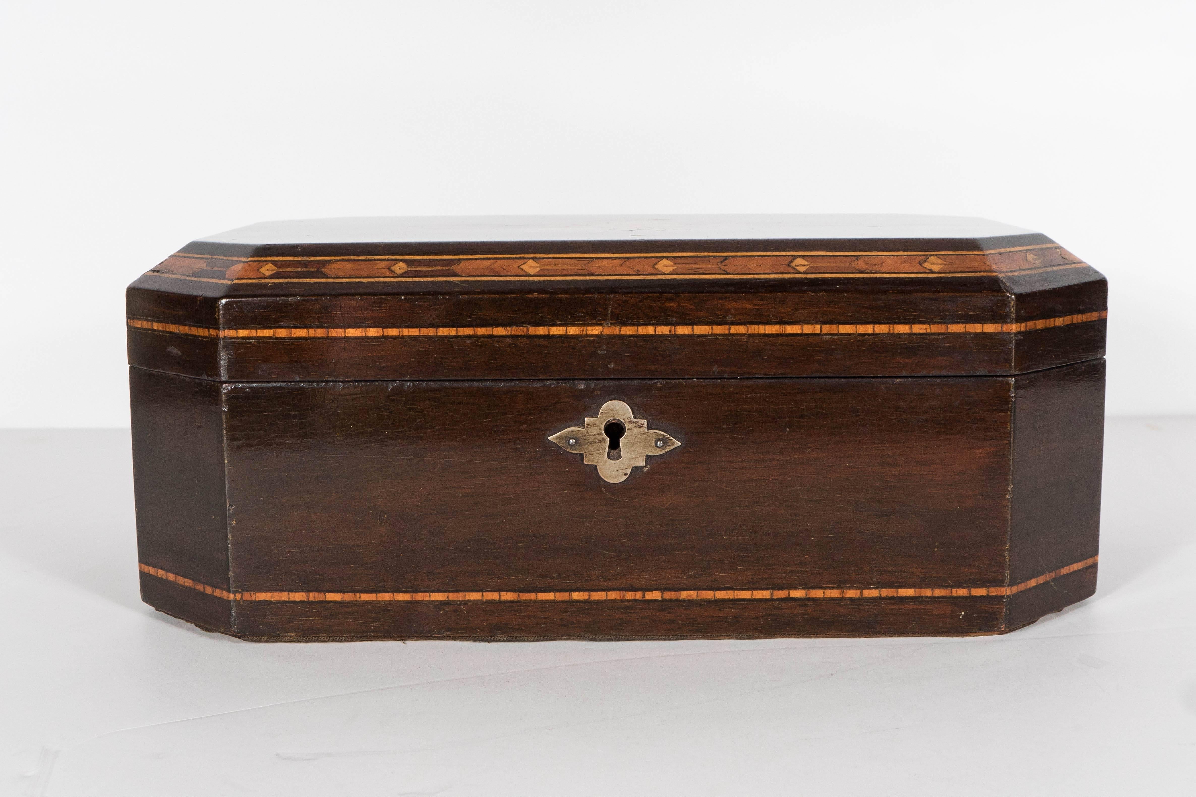 This exquisite mahogany box features an elongated octagonal form with inlaid detailing of exotic walnut, holly and rosewood. The center of the box is inlaid with a rose and branch motif. It also includes a hand-forged tin interior and a recurring