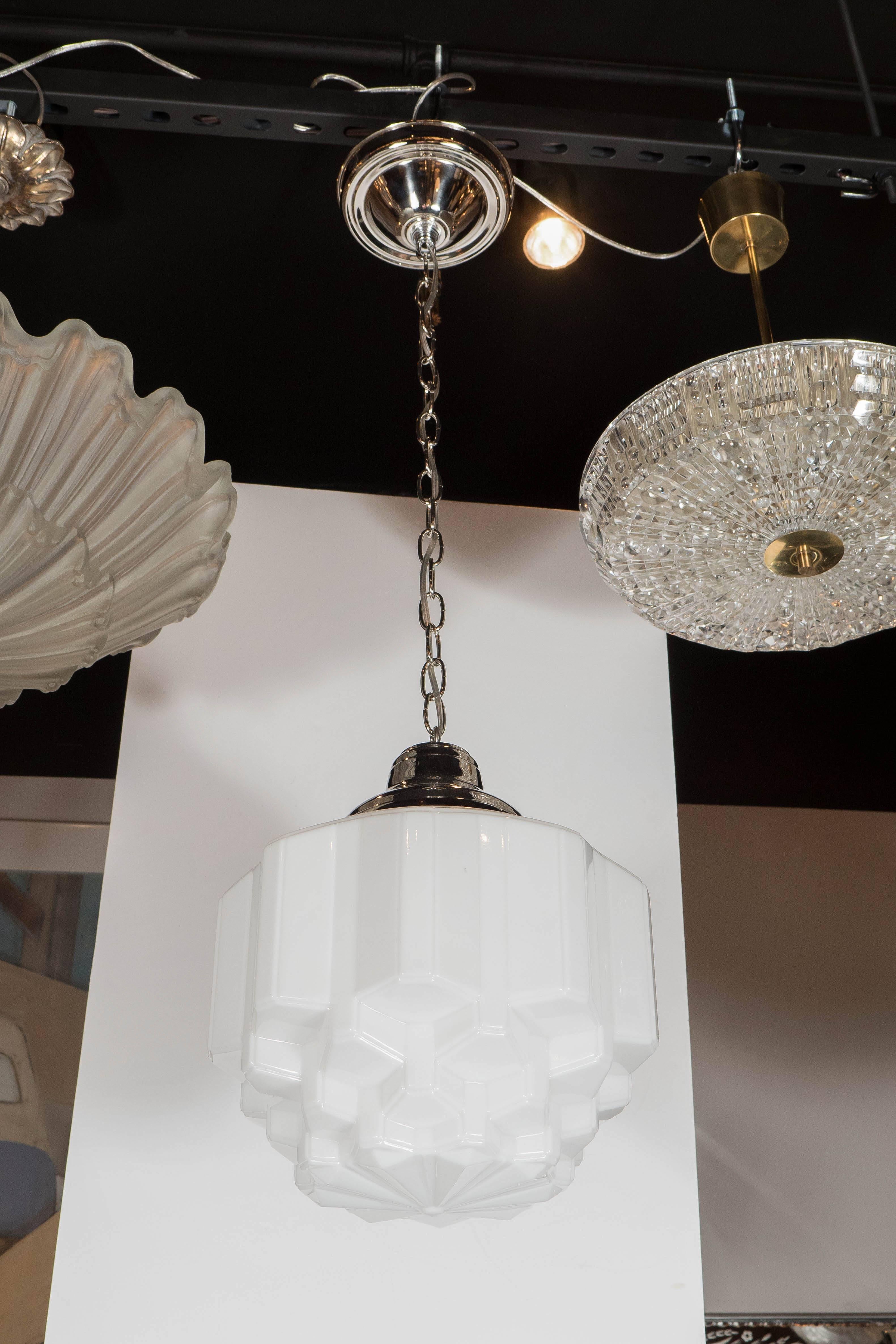 This Art Deco pendant chandelier is made of hand molded white milk glass with skyscraper details and has polished nickel fittings. When viewed from underneath is has a honeycomb-like structure. It can also be used as a flush mount chandelier and has