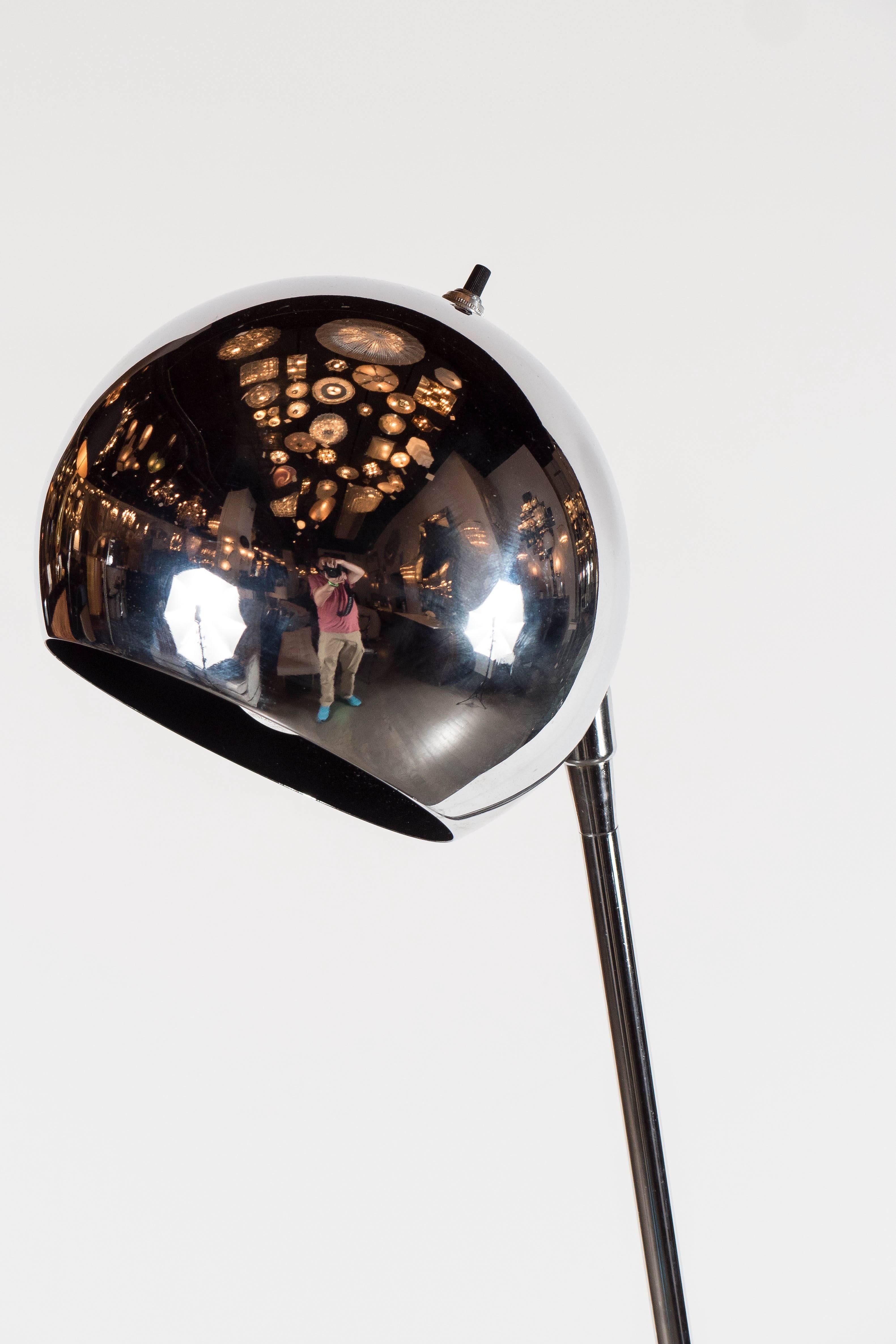 This adjustable floor lamps by the noted designer Robert Sonneman features a base in textured black enamel steel with an adjustable chrome stem with a chrome ball fitted for a Classic light bulb. It ball of the floor lamp has a black enamel