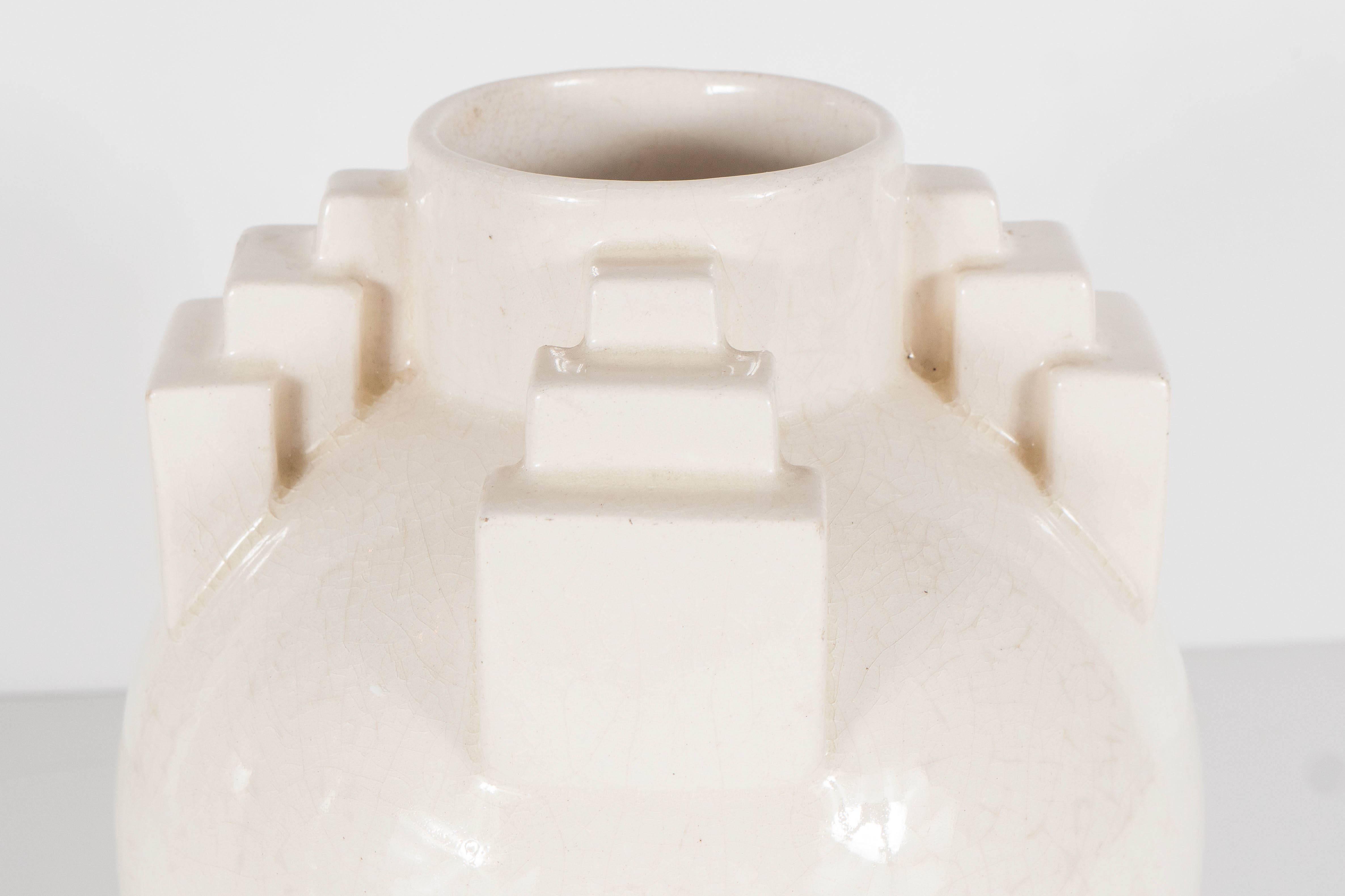 Ce vase sophistiqué Art déco à glaçure craquelée de St. Clement présente une forme ronde avec des détails de gratte-ciel décorant l'ouverture du vase, ce qui confère à l'ensemble du design équilibre et intérêt. Il est de couleur ivoire et est en