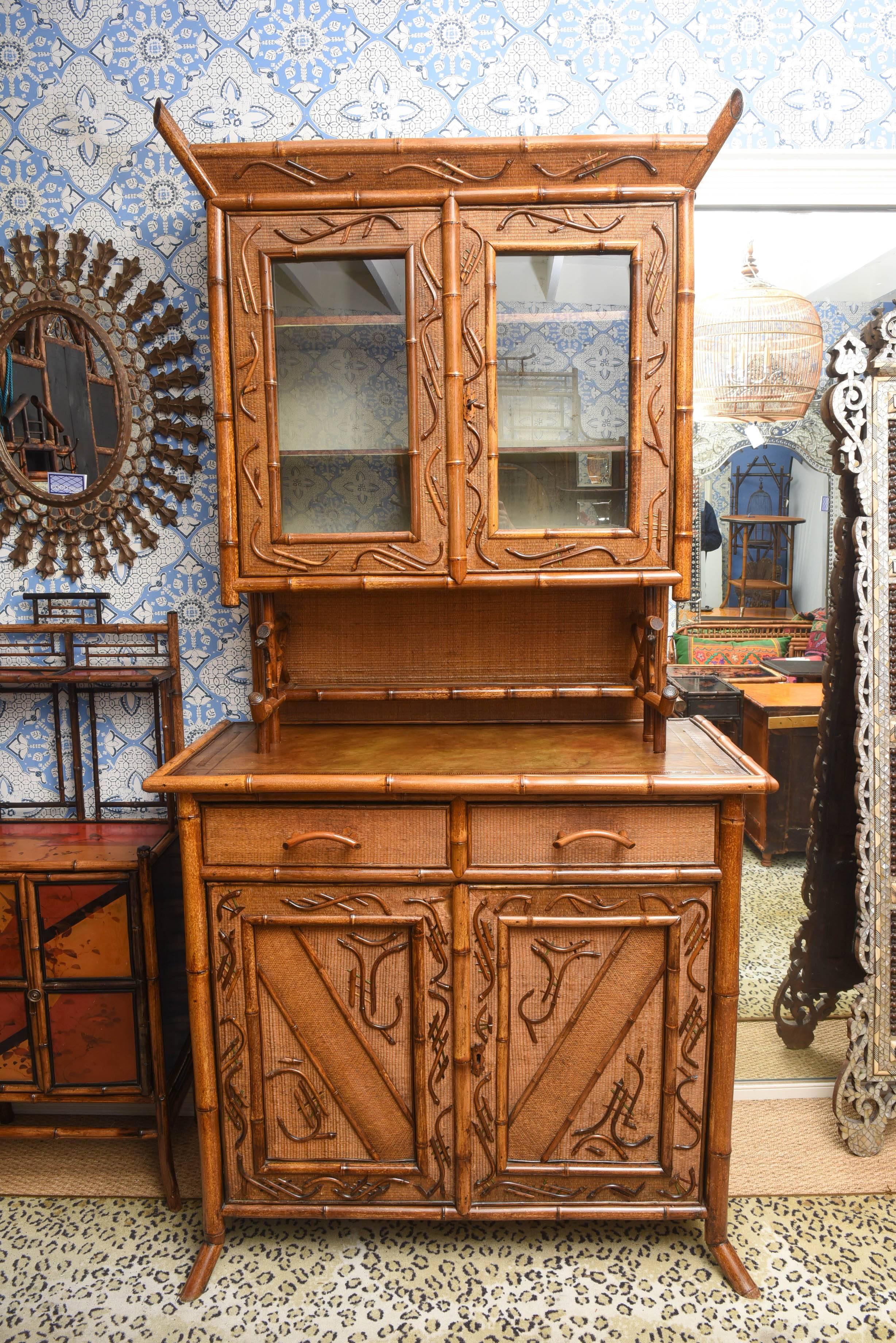 Late 19th or early 20th century English two-part bamboo cupboard, the upper cabinet with glass fronted storage, over a two drawer, two door base cabinet with tooled leather top, the door panels with applied bamboo decoration, Measures: 92