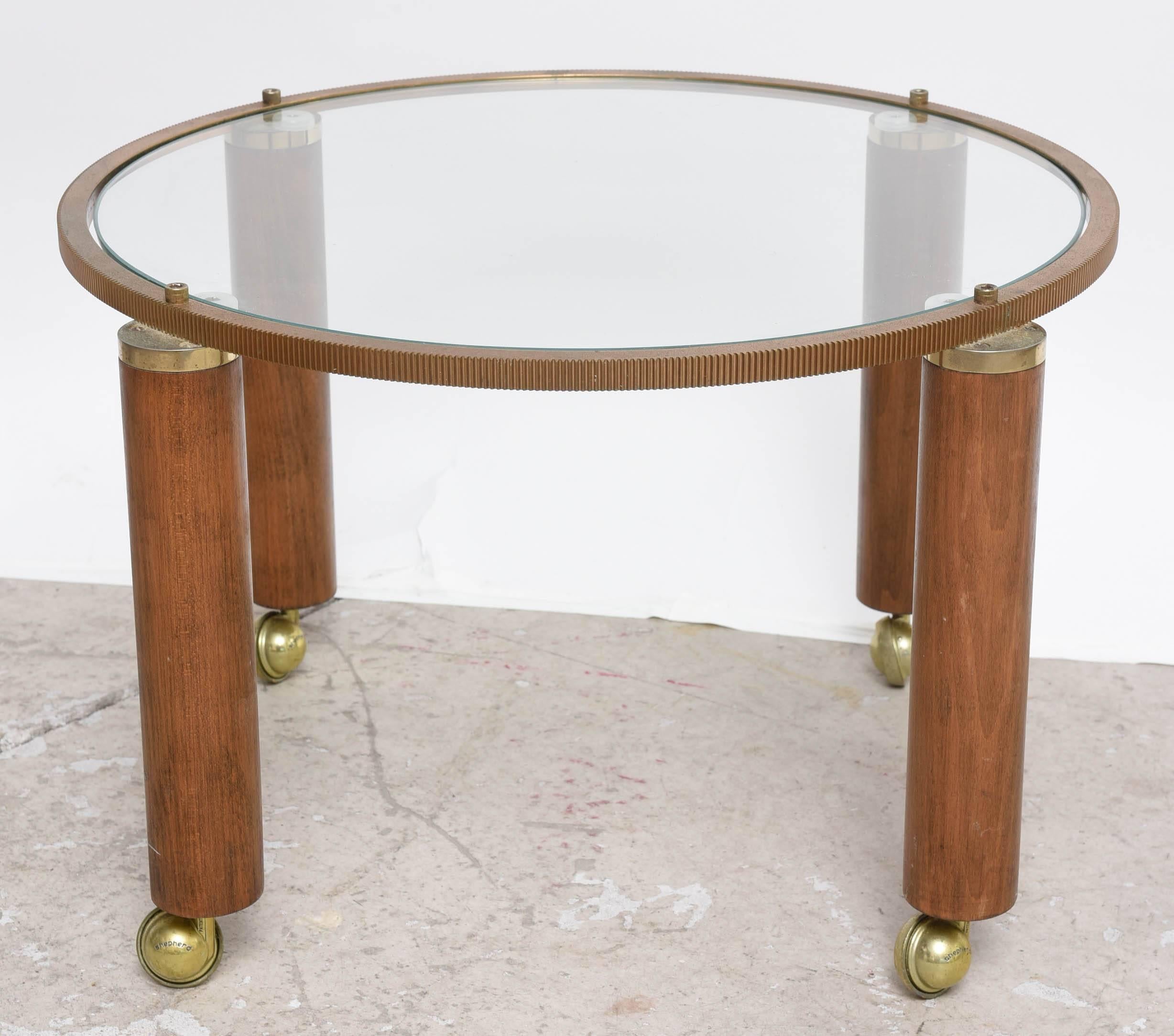 Pair of Mid-Century Modern side tables. The wood legs are on casters and the construction is mixed of metal and wood. The stylized mechanical in copper finish ring top holds a clear 20