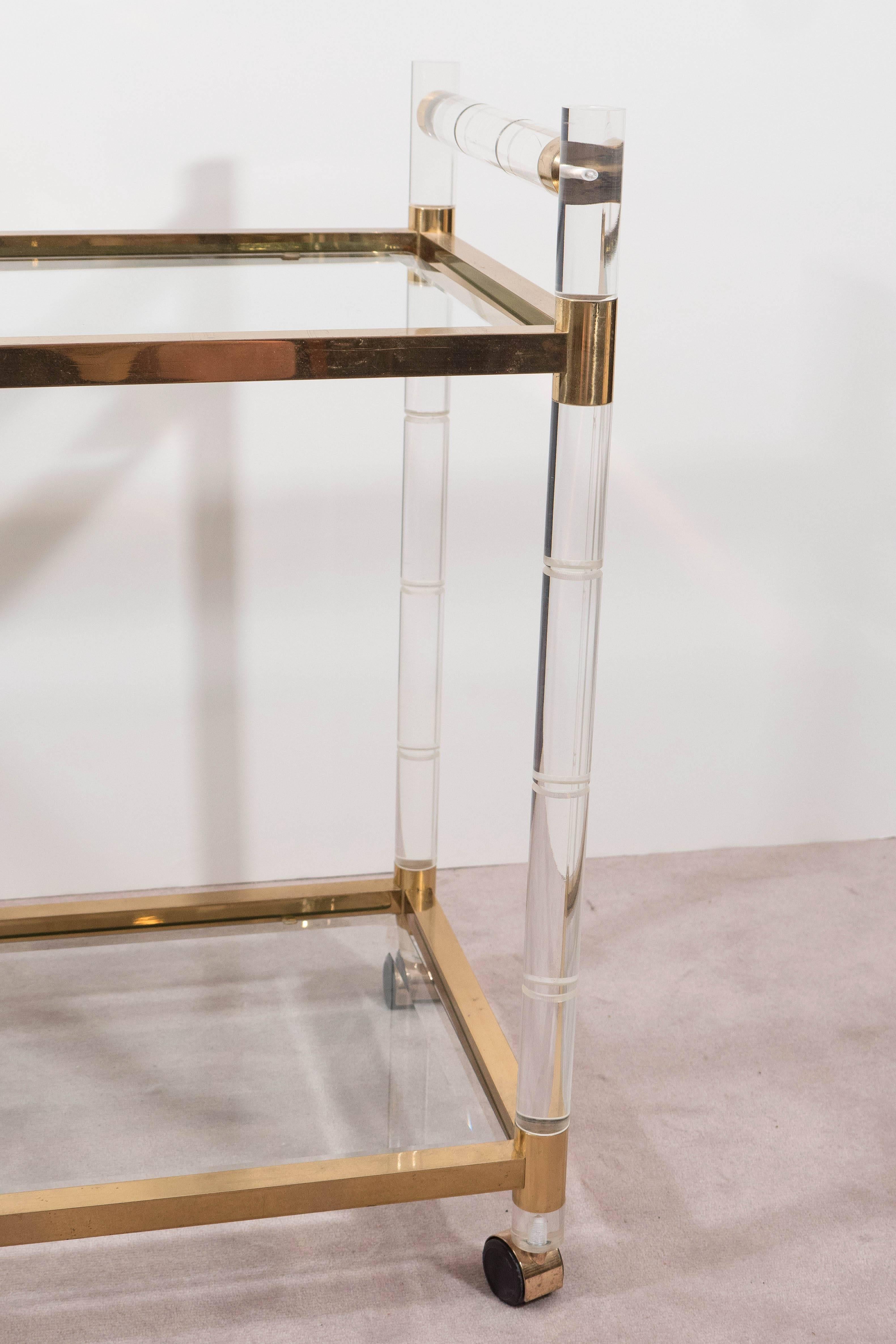 A bar and serving cart by designer Charles Hollis Jones, with two-tier glass tops, inset against polished brass frames and faux bamboo legs and bar handles in Lucite, on casters, circa 1960s-1970s Very good condition, minimal wear consistent with