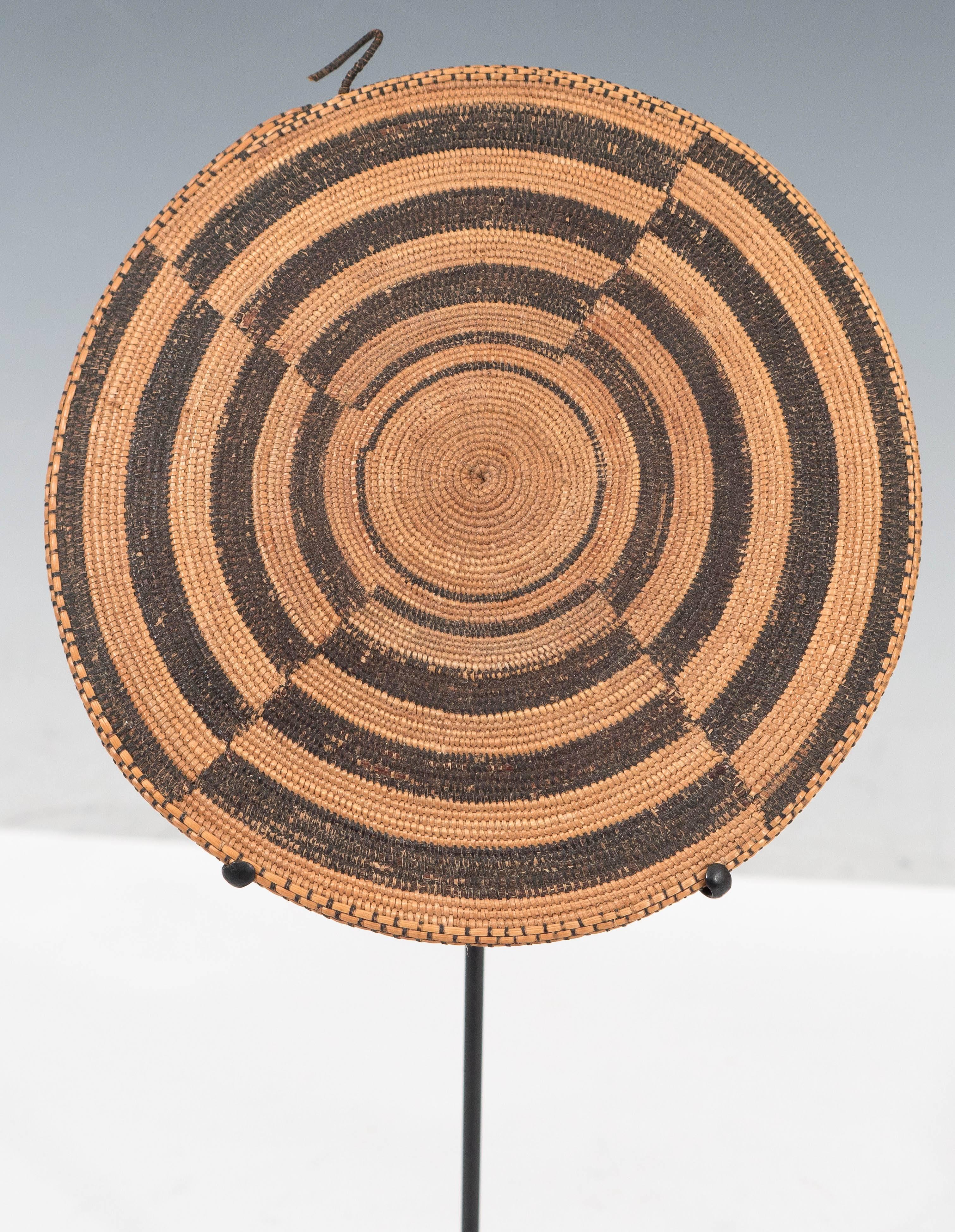 A hand-woven rattan cane disc, with dyed black patterns, supported on a metal stand, will add a natural and environmental touch to the interior setting. Very good condition, consistent with age.
