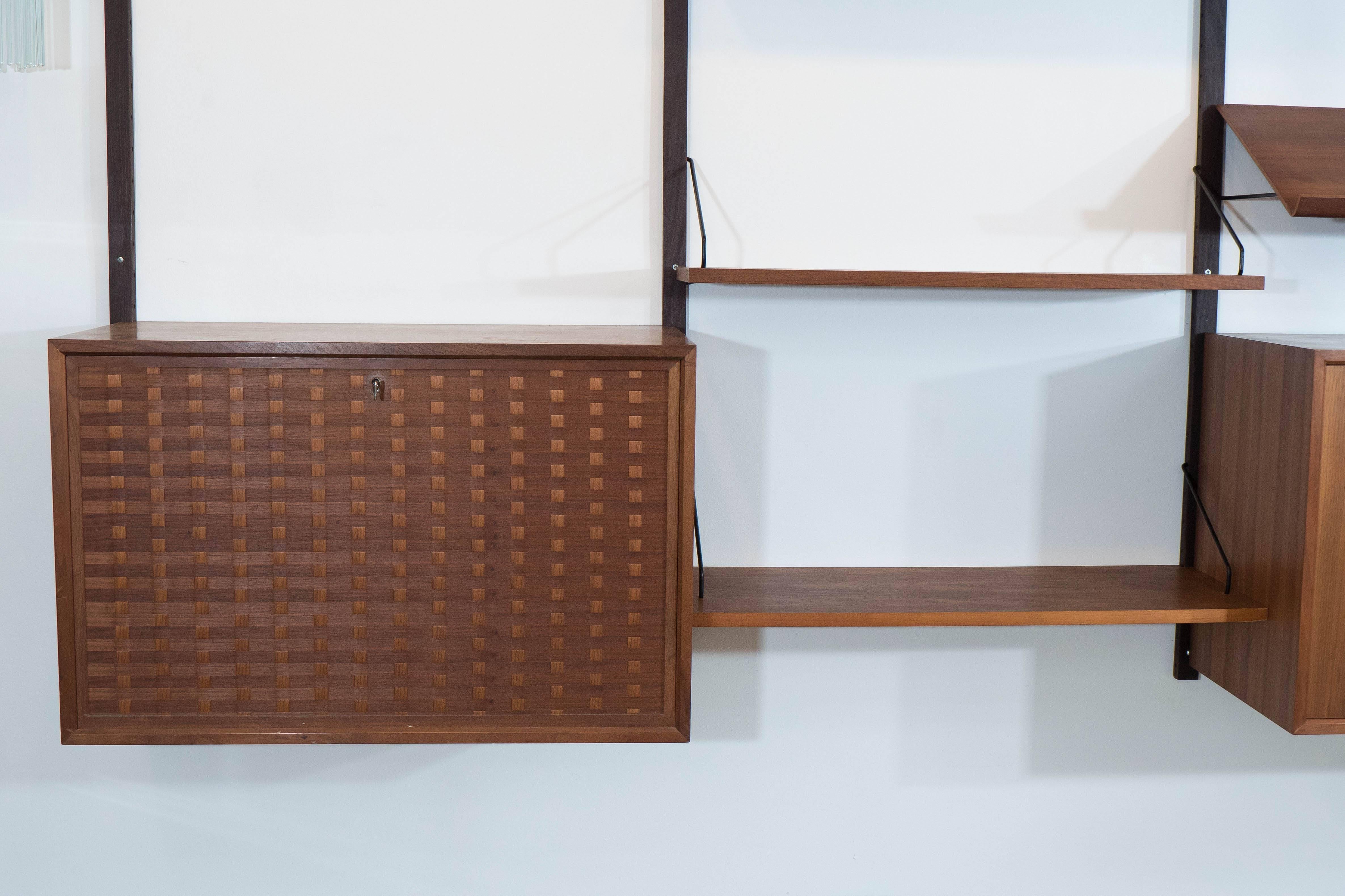 This adjustable walnut shelving system was designed in the 1960s by Danish interior architect Poul Cadovius. The four wall-mountable supports hold three separate cabinets, with two wooden doors, two glass sliding doors and two interior glass shelves