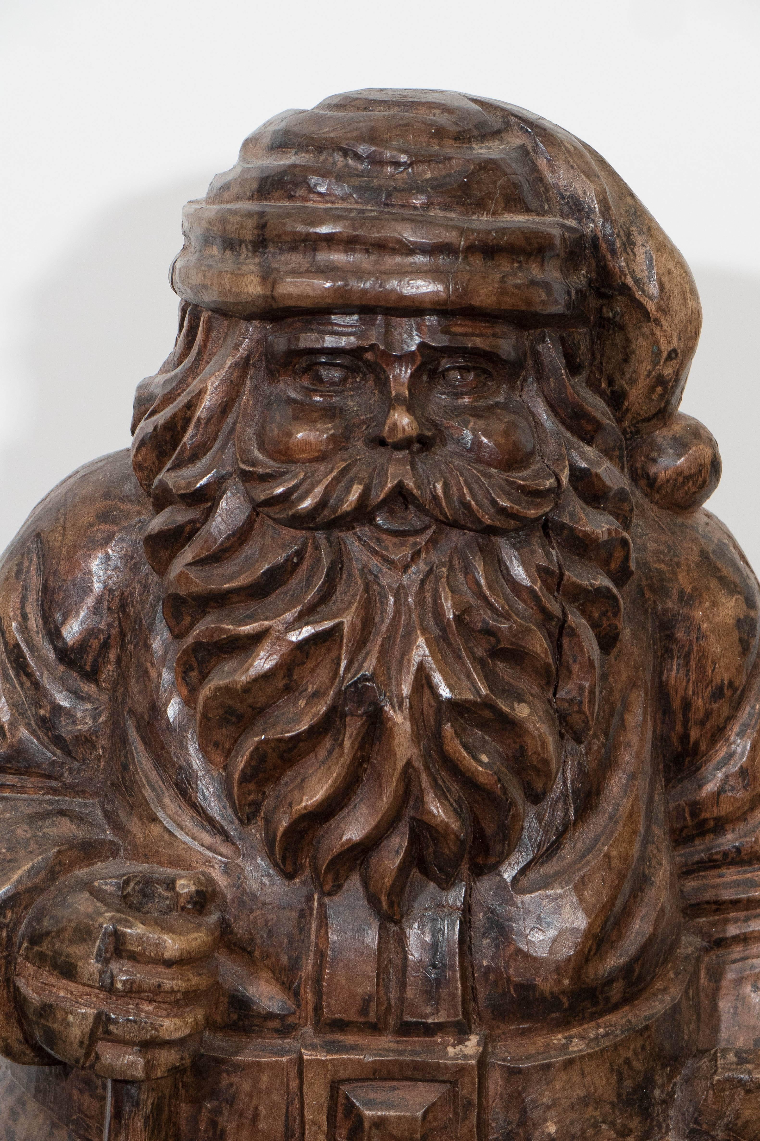 A solid carved wood Santa, produced circa 1920s, used originally as a mold for making papier mâché toys and decorative arts. Santa is positioned with his bag of toys. Mold shows signs of use, such as knife cuts, cracks and chipping, giving the piece