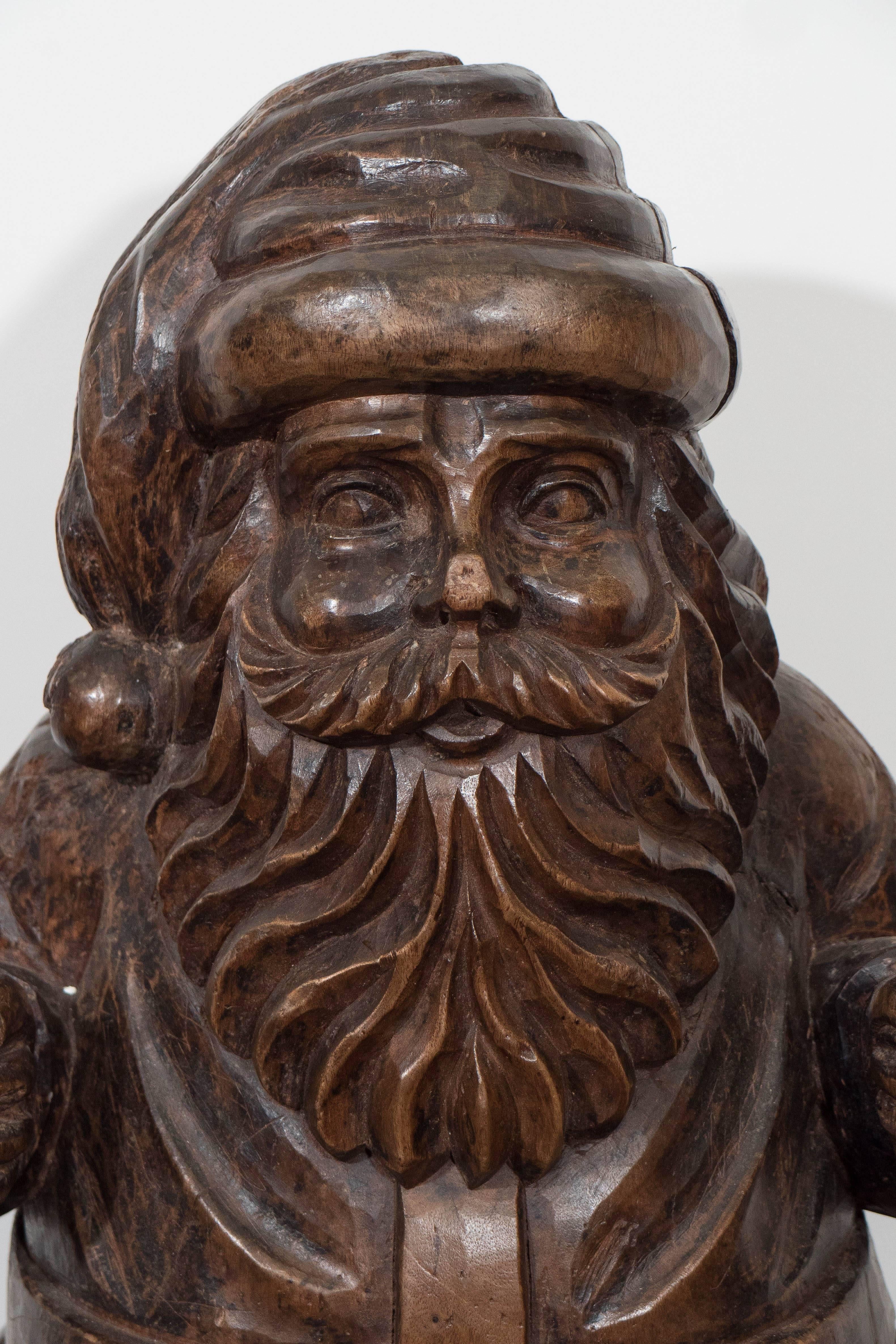 Solid carved wood Santa, used originally as a mold for making papier mâché toys and decorative arts. Santa is positioned as if standing in his sleigh, holding the reins as he steers his reindeer. The mold shows signs of use, such as knife cuts,