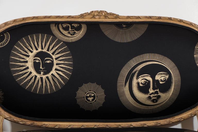 A 19th century settee, in the manner of Louis XVI, with a painted and distressed wood finish, newly upholstered in vintage Piero Fornasetti cotton fabric, detailed with depictions of the sun and moon, iconic of the Italian designer's oeuvre. Very