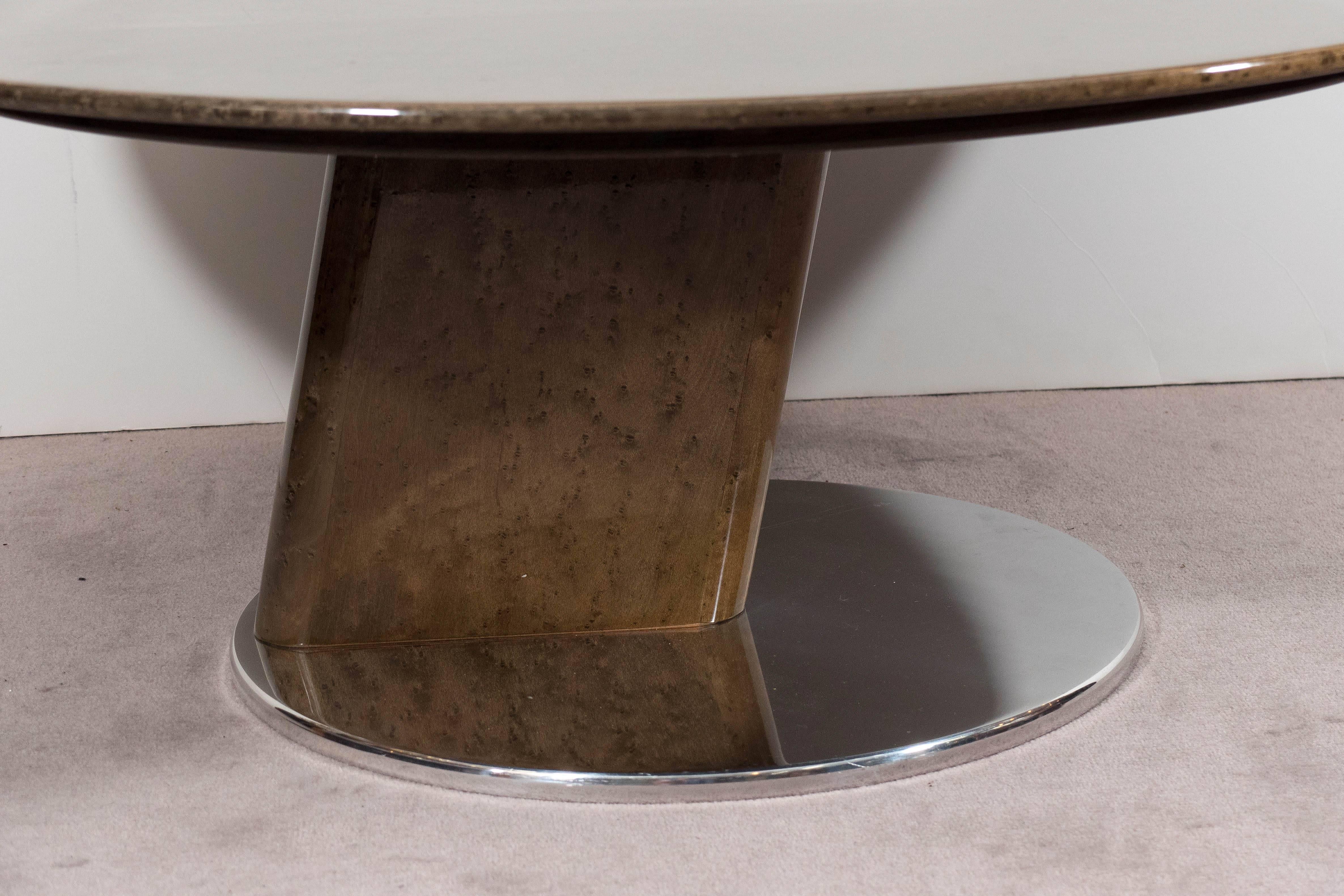 A round, birds-eye maple coffee table by Saporiti, lacquered to a gleaming finish, above a smaller circular polished steel base. The base features a unique triangular shape joining the two circles. Good condition, consistent with age and use, with a