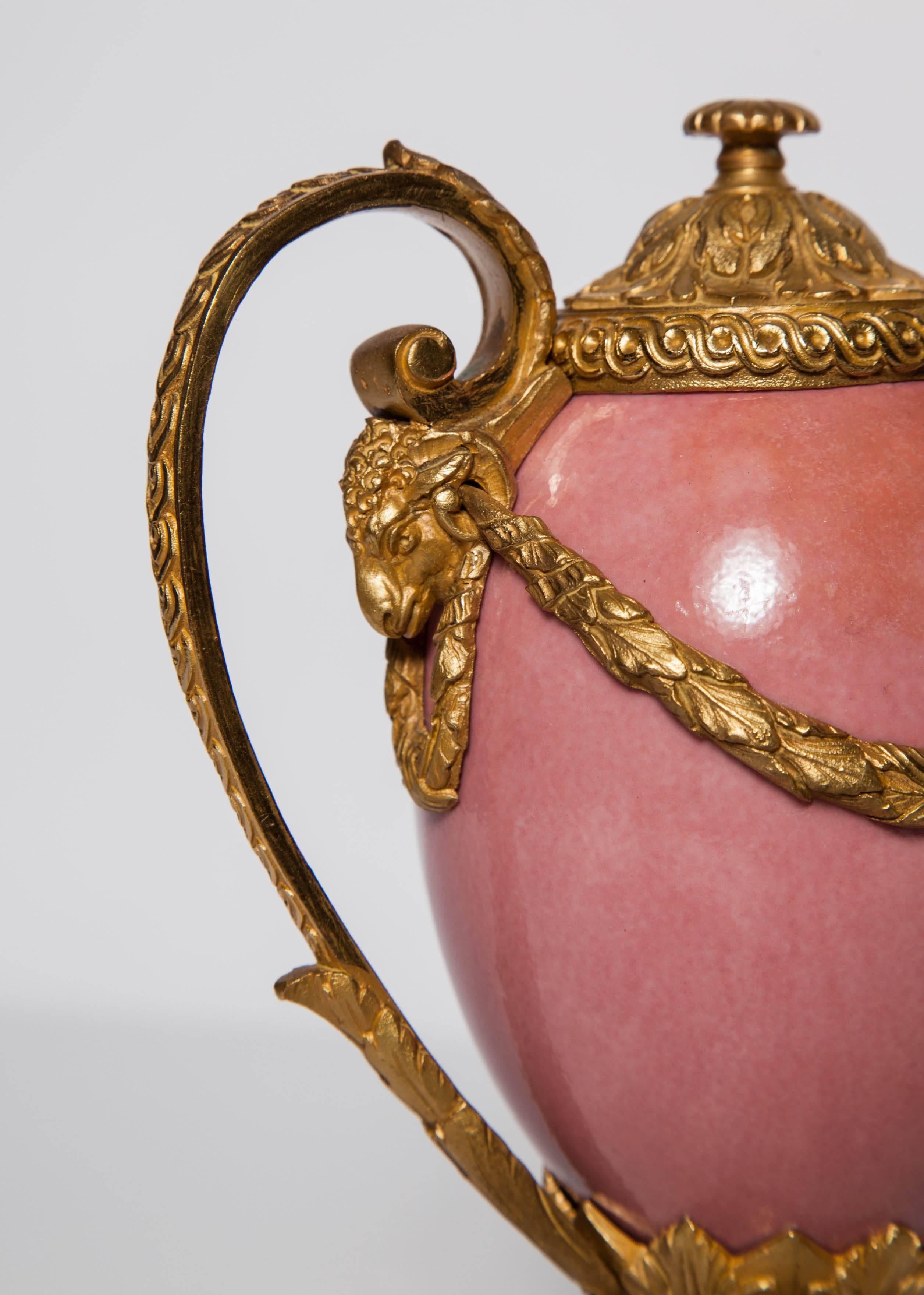 A fine pair of antique English neoclassical porcelain and doré bronze mounted two handled Cassolettes. Each having a pair of ram's heads terminating and connecting each handle to the body, all resting on a double tier stepped pedestal base.