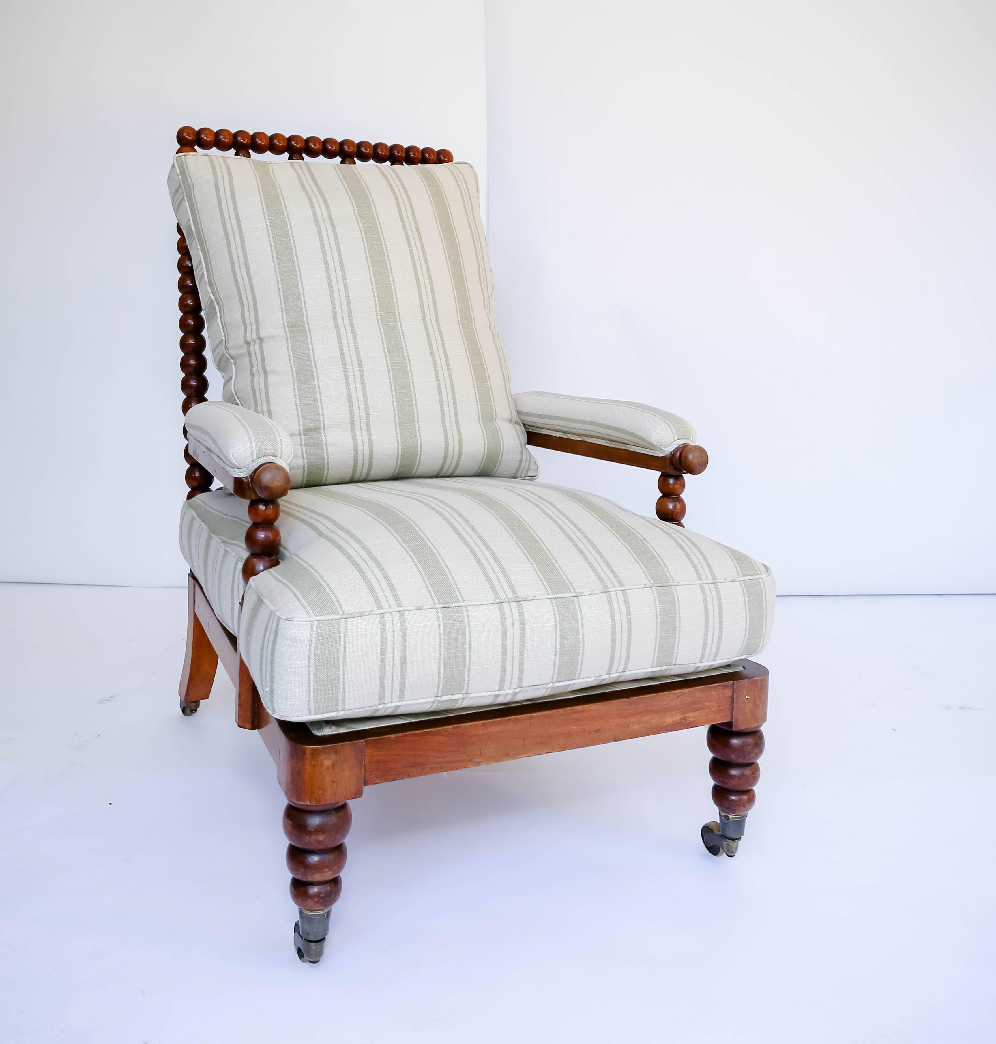 Antique English bobbin-turned wooden armchair with single crest-rail and four spindle-slat back rest.  Front turned and rear splayed legs fitted with brass roller castors, striped linen upholstery. 