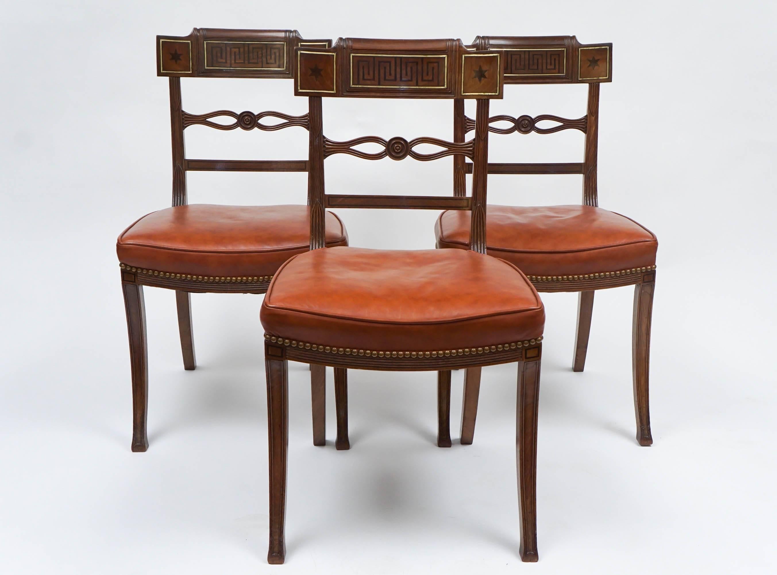 Rare and remarkable set of six, circa 1805, neoclassical English Regency dining chairs having mahogany frame of klismos form, the crest rail divided in three sections with 'Greek key' and star ebony inlay inside brass inlaid borders surmounting