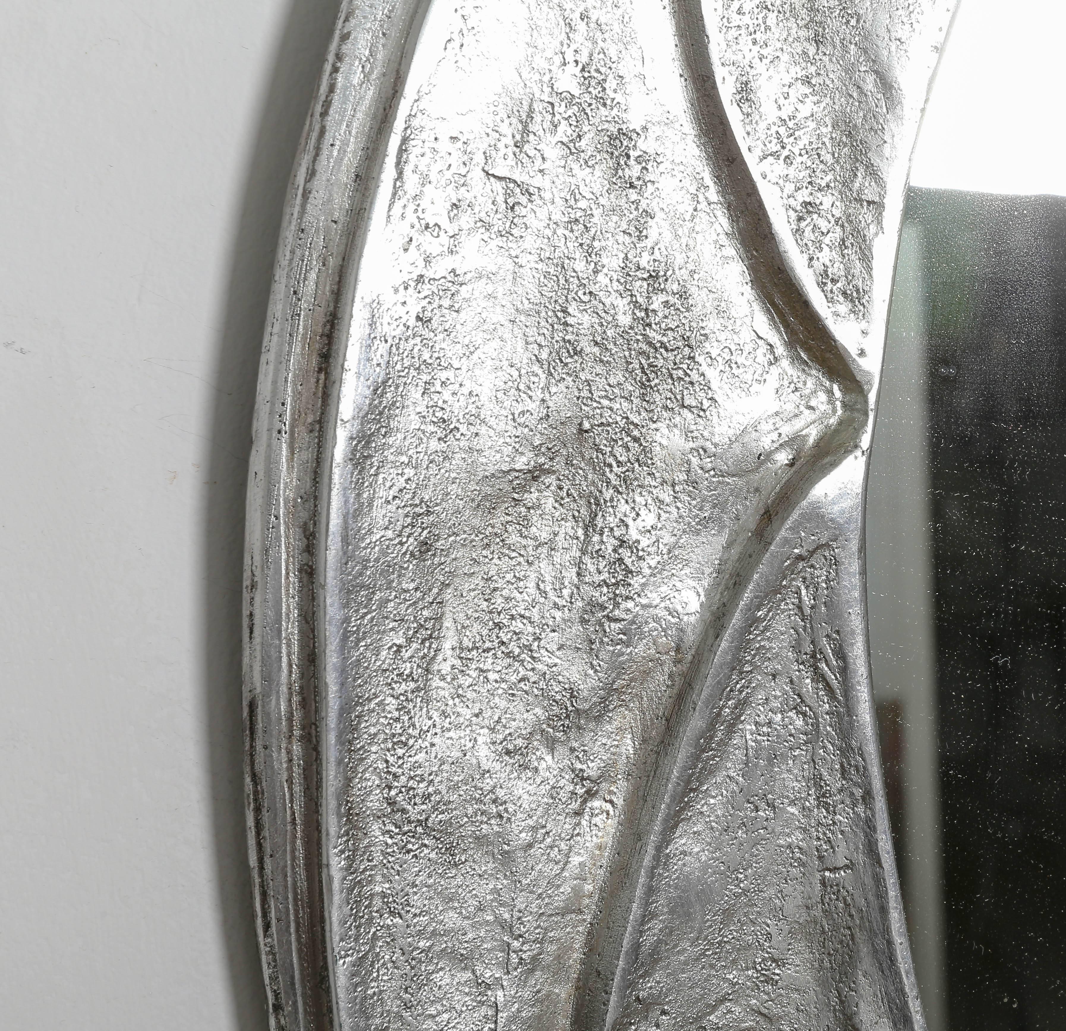 Asymetrical ovoid mirror with textured relief aluminium surround.