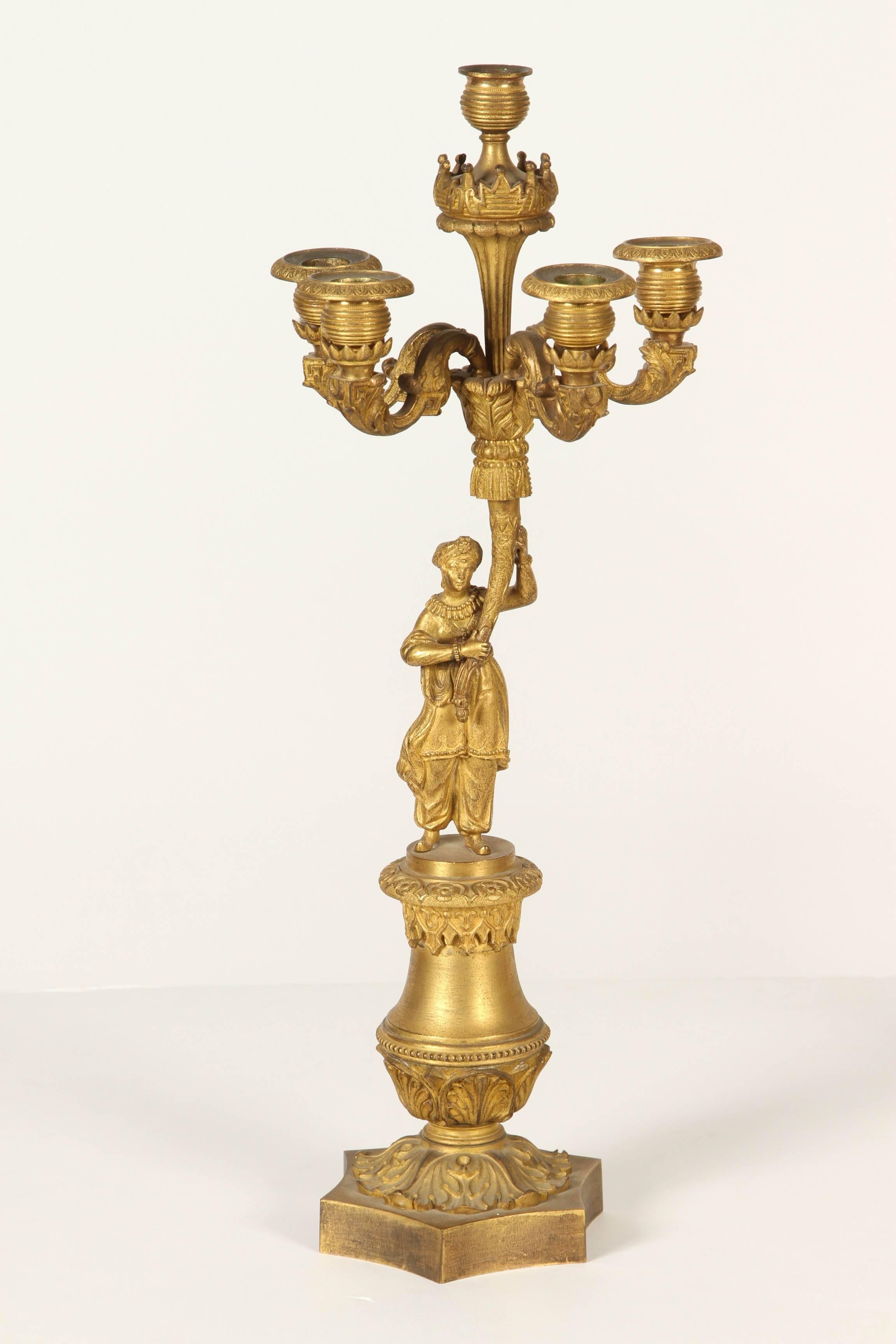 Cada uno de estos candelabros tiene cuatro luces rematadas por una luz adicional y está sostenido por un hombre y una mujer vestidos de forma exótica. 