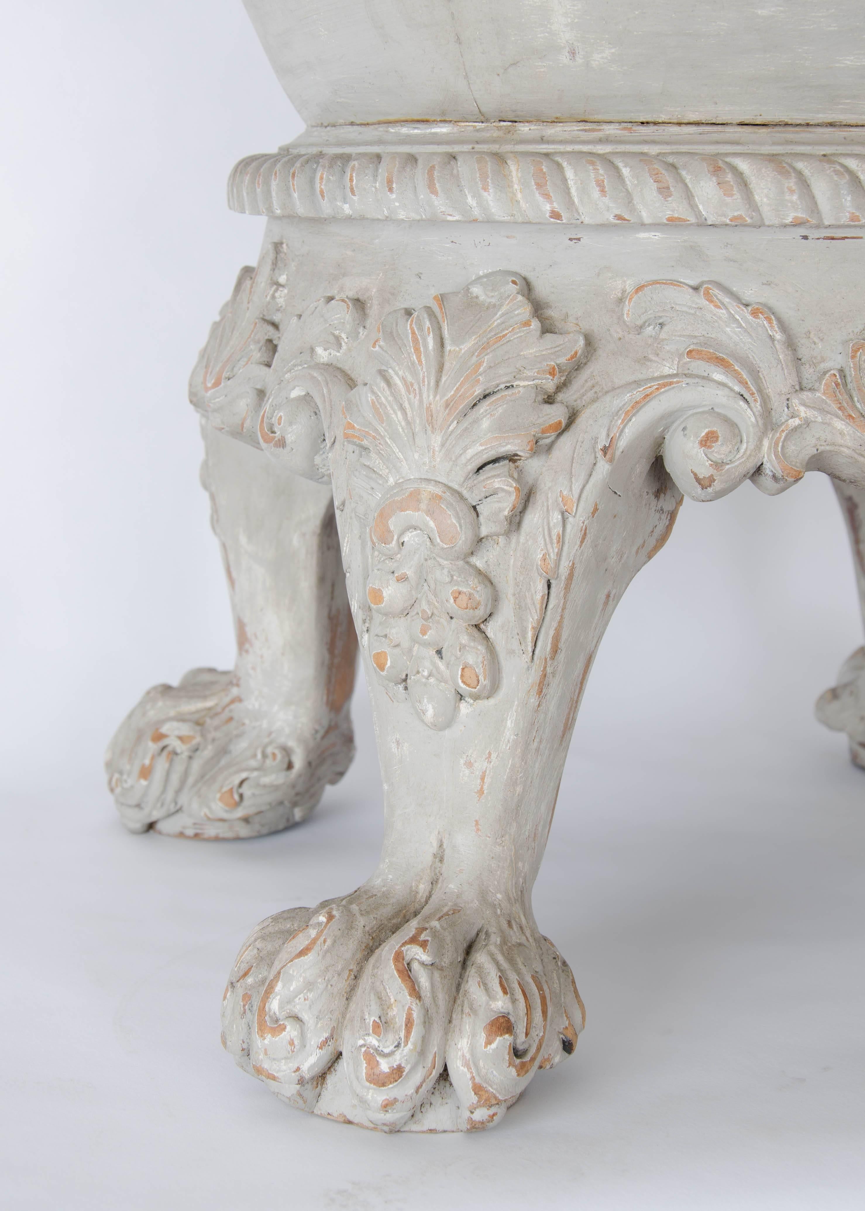 An early 20th century painted wine coller with carved elliptical lip over upturned trapezoid shaped body with central banding on four heavily carved hiary paw feet with acanthus leaf detailing.