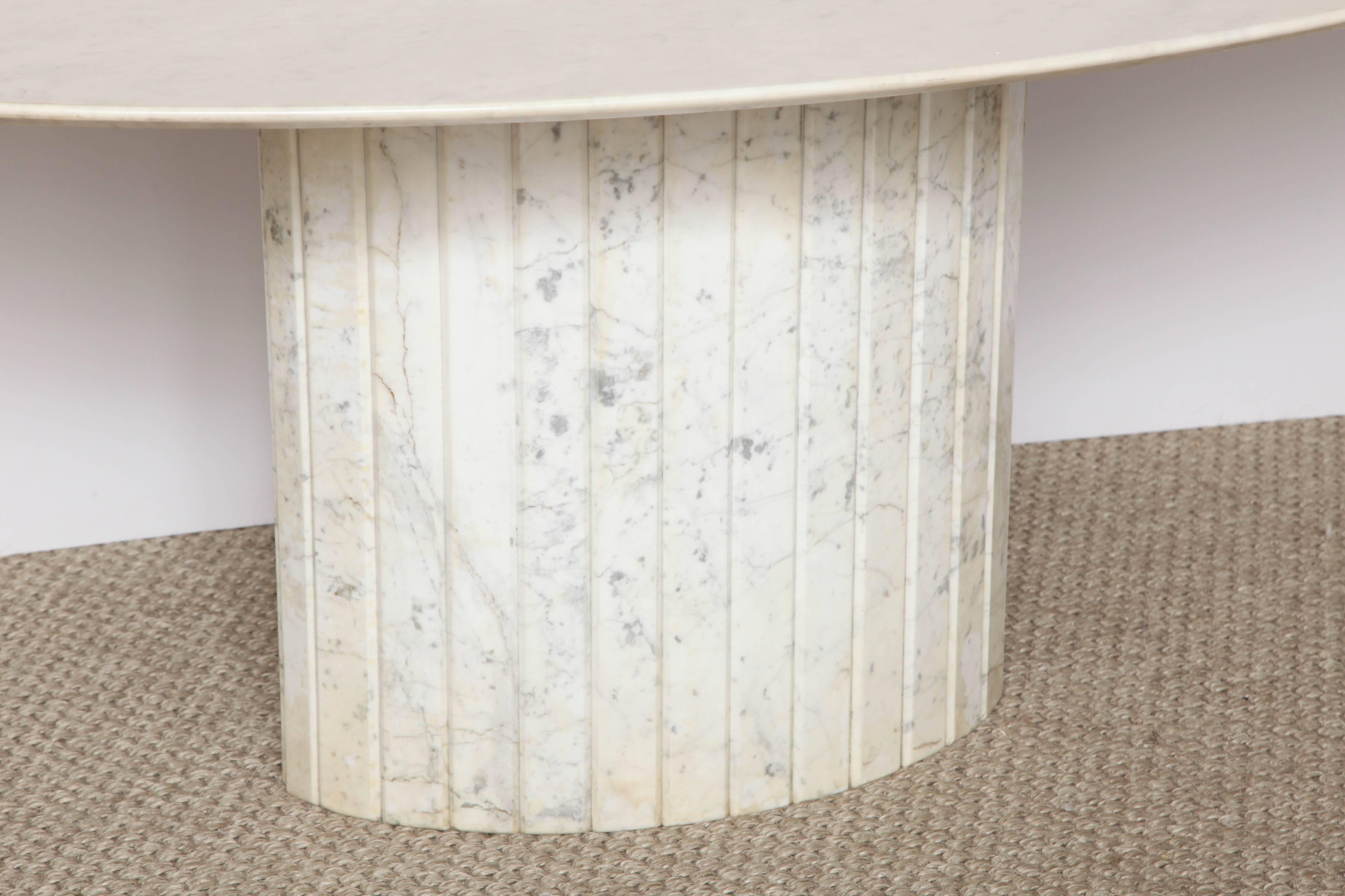 A fabulous dining table consisting of a Carrara marble top on a reeded oval base.