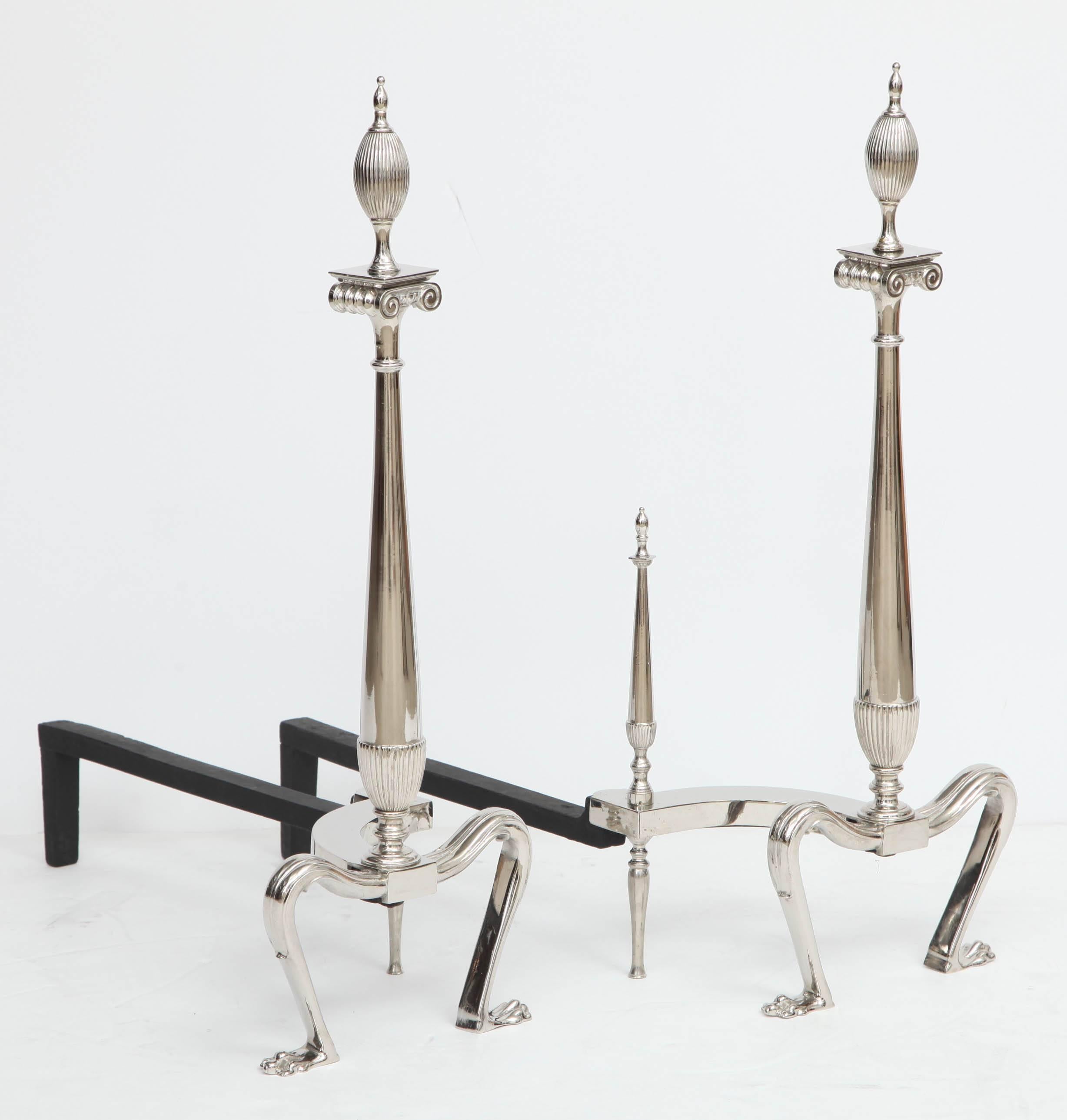 Pair of stylish Art Deco polished nickel andirons with fluted finial tops on ionic capital forms.