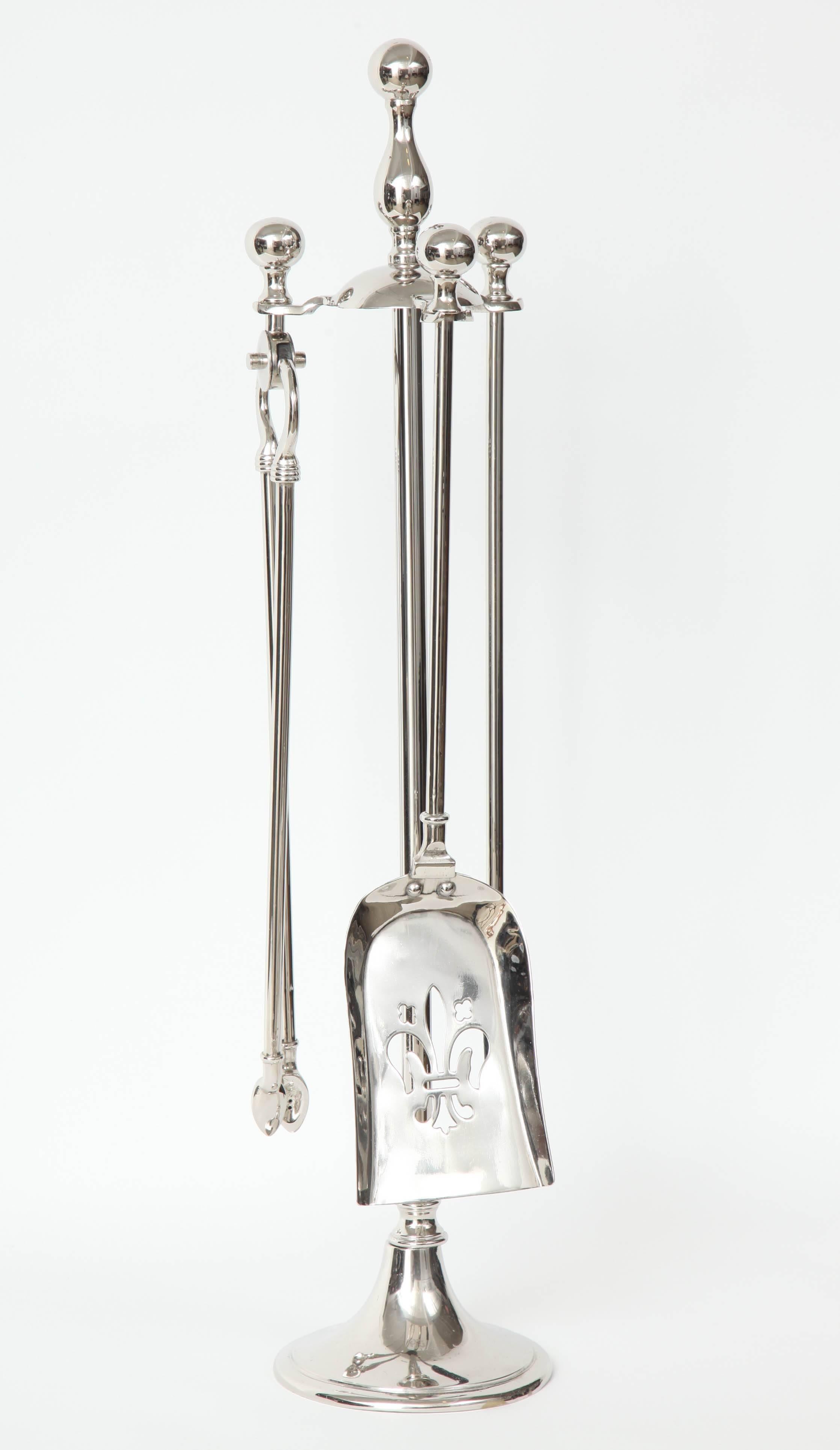 Mid-Century set of polished nickel fireplace tools composed of a stand, tongs, poker and a shovel with a fleur-de-lis cut-out.