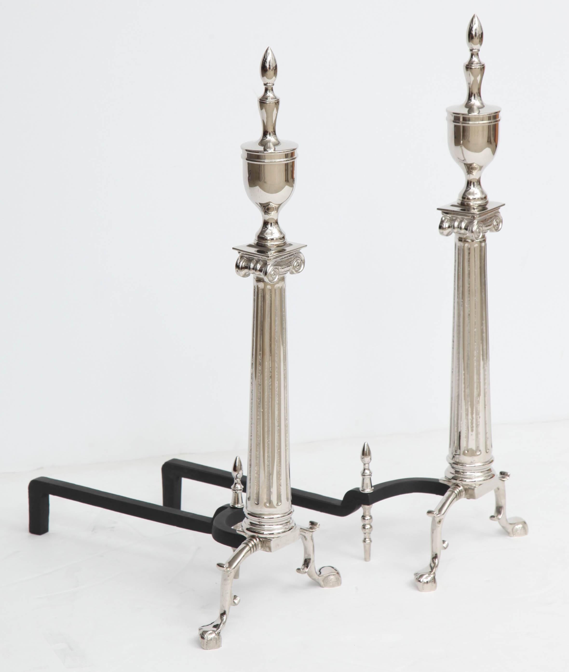 Pair of grand polished nickel andirons with a traditional ionic column form with a stately urn finial.