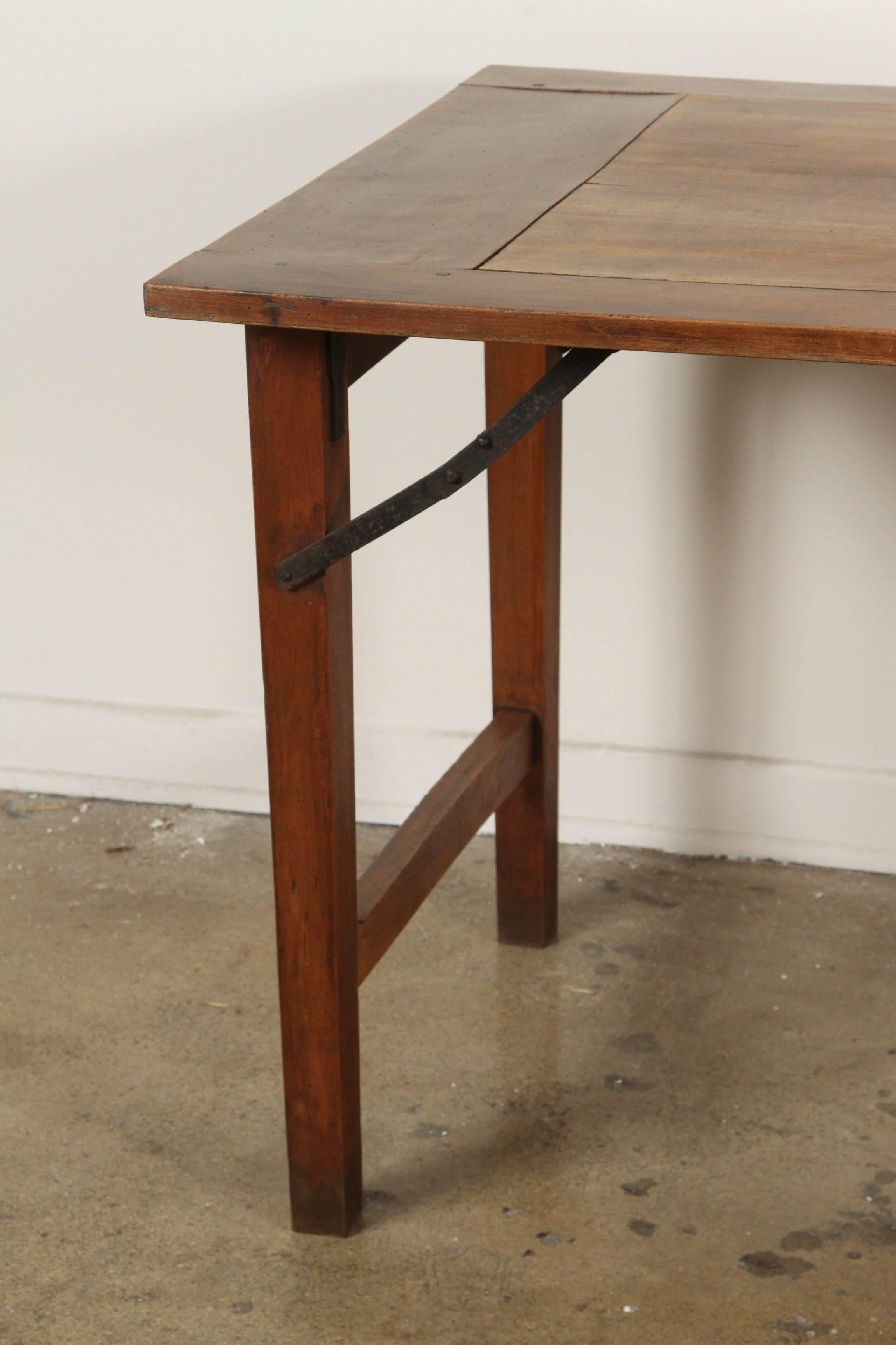 Late 19th-century French walnut wood table with collapsable folding legs. Perfect as a dining table, workbench, or long desk, the exposed mechanics of the iron arms provide an industrial accent to the otherwise provincial nature of this