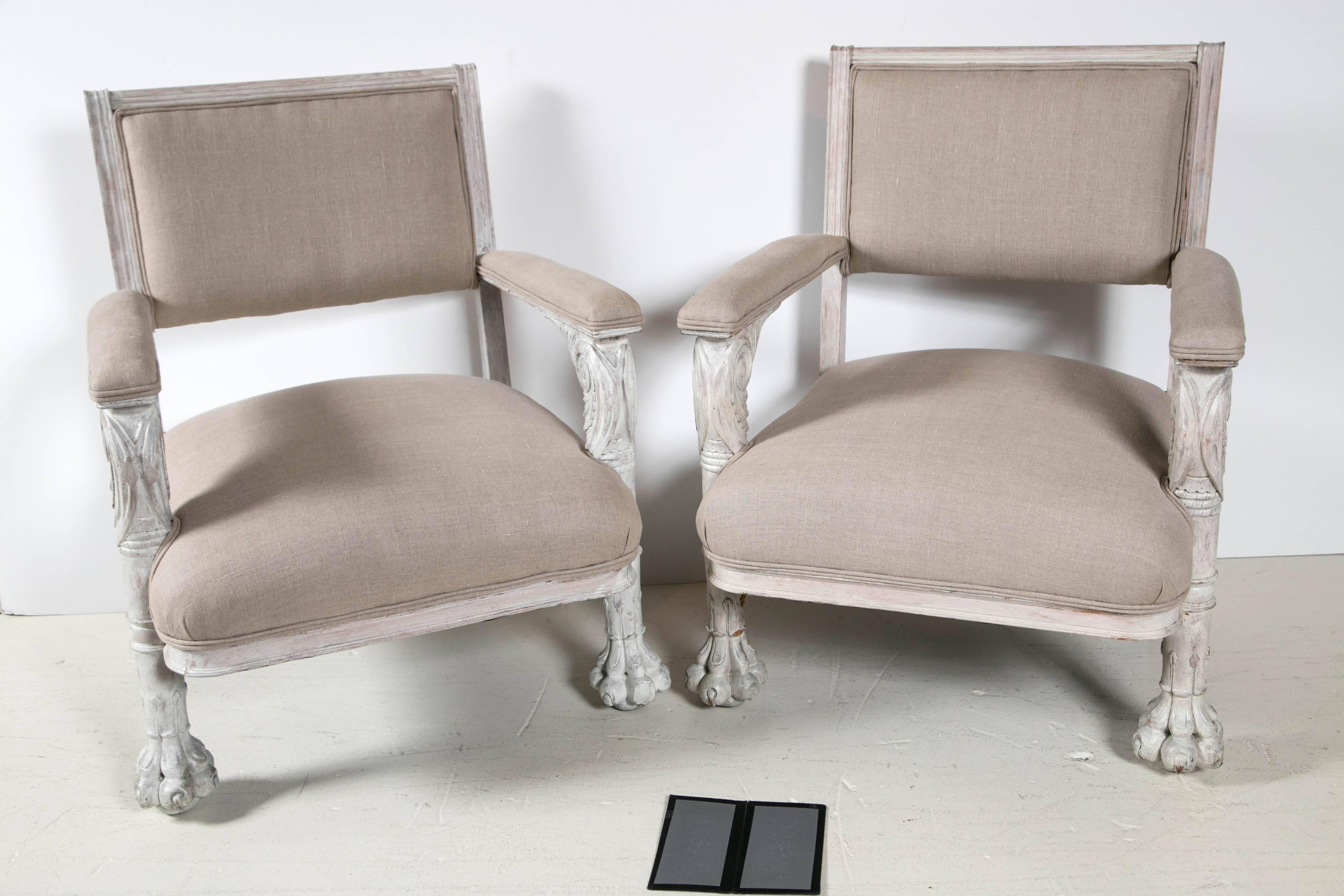 Pair of white carved armchairs, painted frames, light cream finish, squared backs, carved arm supports and lion paw feet. Upholstered in Belgian linen. 