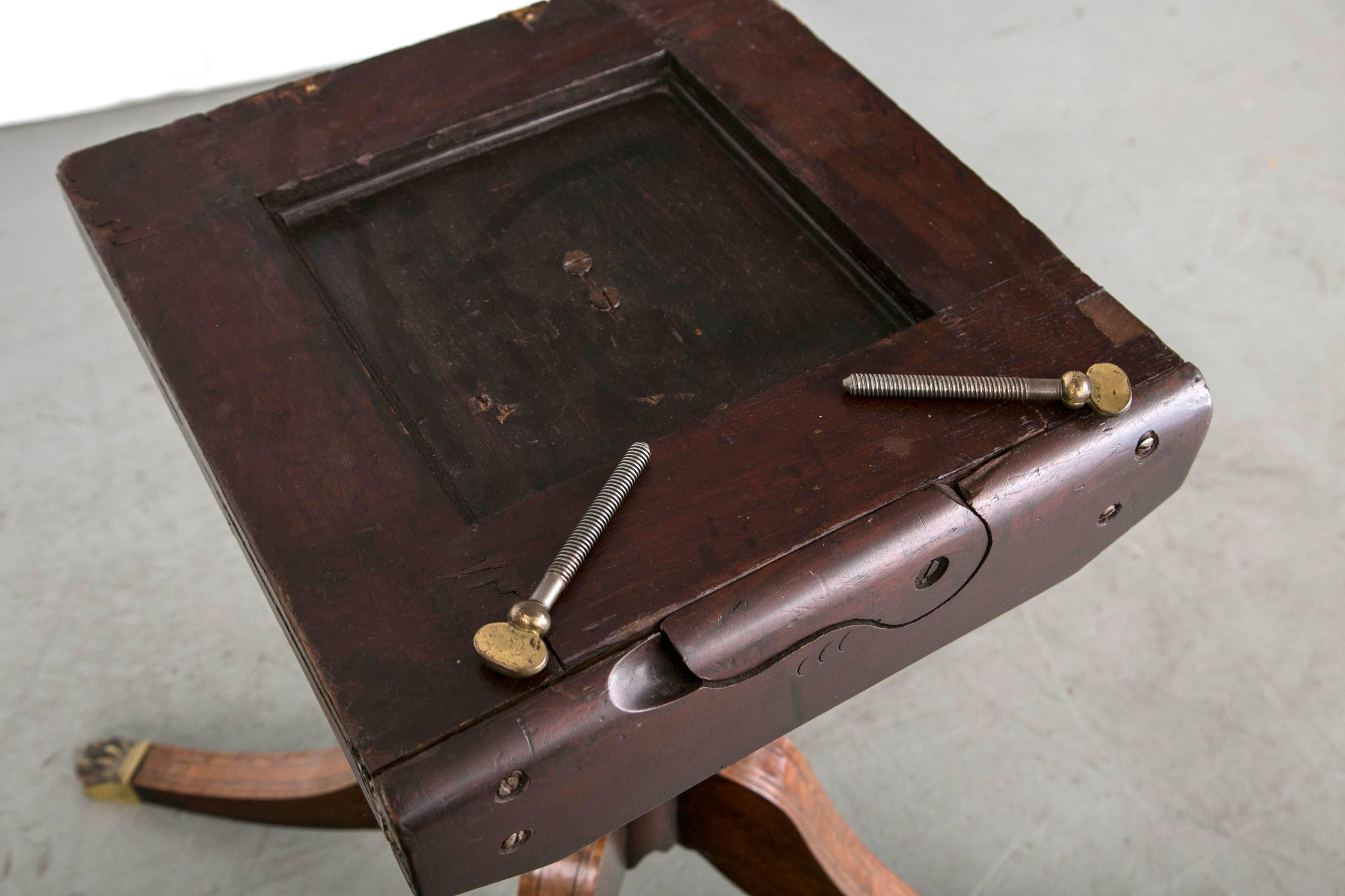 A round pedestal tilt-top table with original brass paw feet. The top.