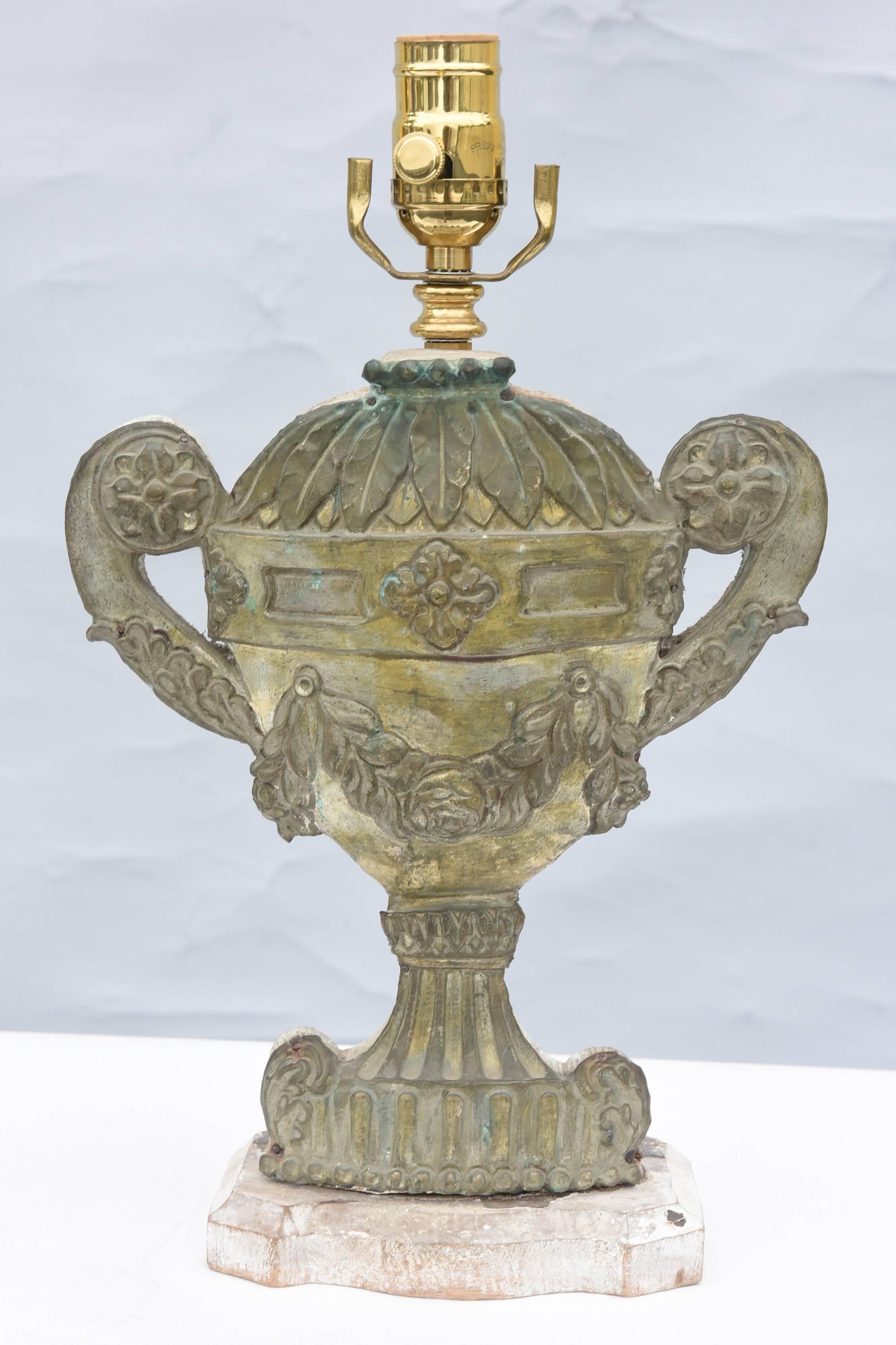 Pair of lamps, of repoussé bronze, each an urn with a cap of laurel leaves, fluted body centered with a rosette, flanked by scrolling handles, decorated by acanthus leaves, on fluted socle and foot; wooden backplate and base.

Stock ID: D6242